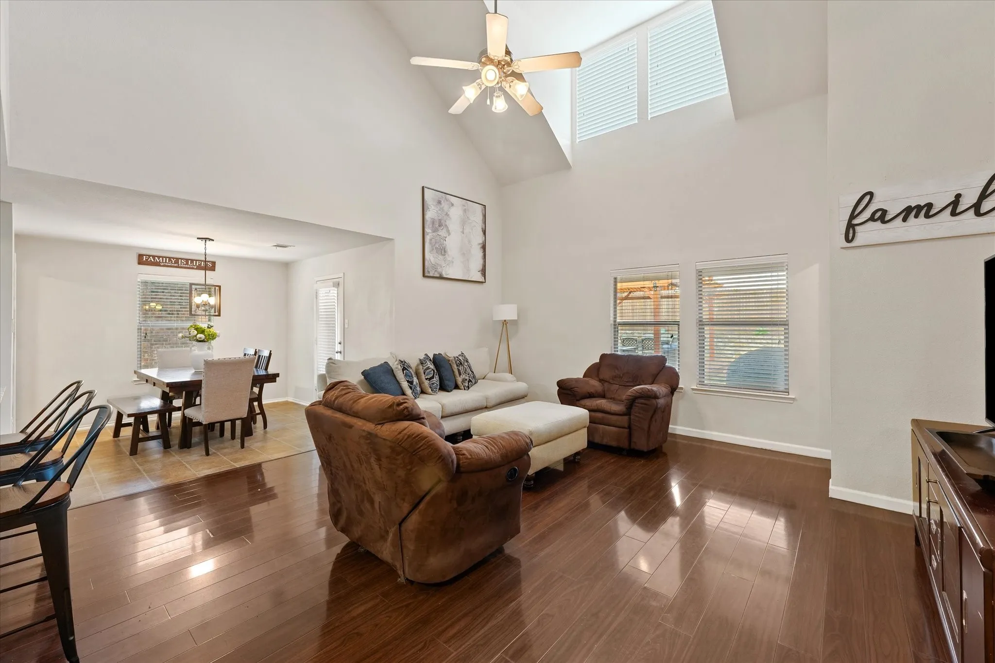 Vaulted ceiling with a ceiling fan, wood-finish flooring, multiple windows, and a recessed dining area with tile flooring