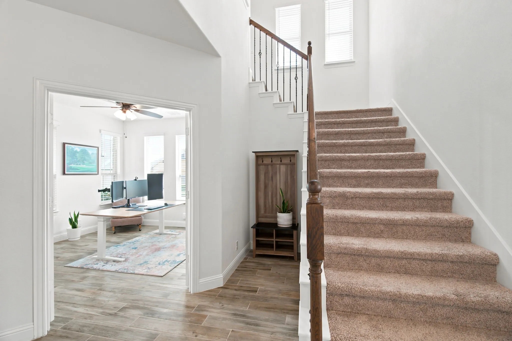 Staircase with carpeted treads and wood handrail, featuring wrought iron balusters