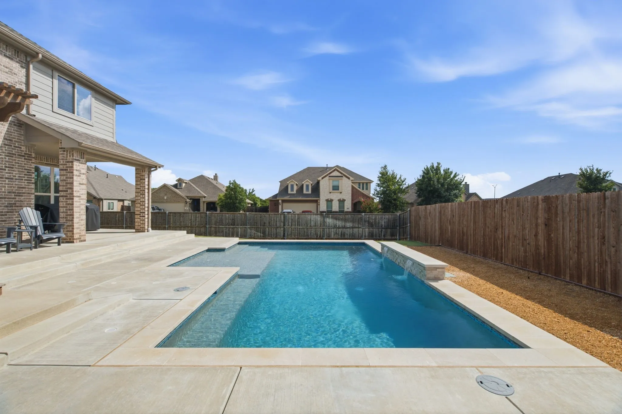 Backyard featuring a rectangular swimming pool, concrete patio, covered patio with brick columns, and a wood privacy fence