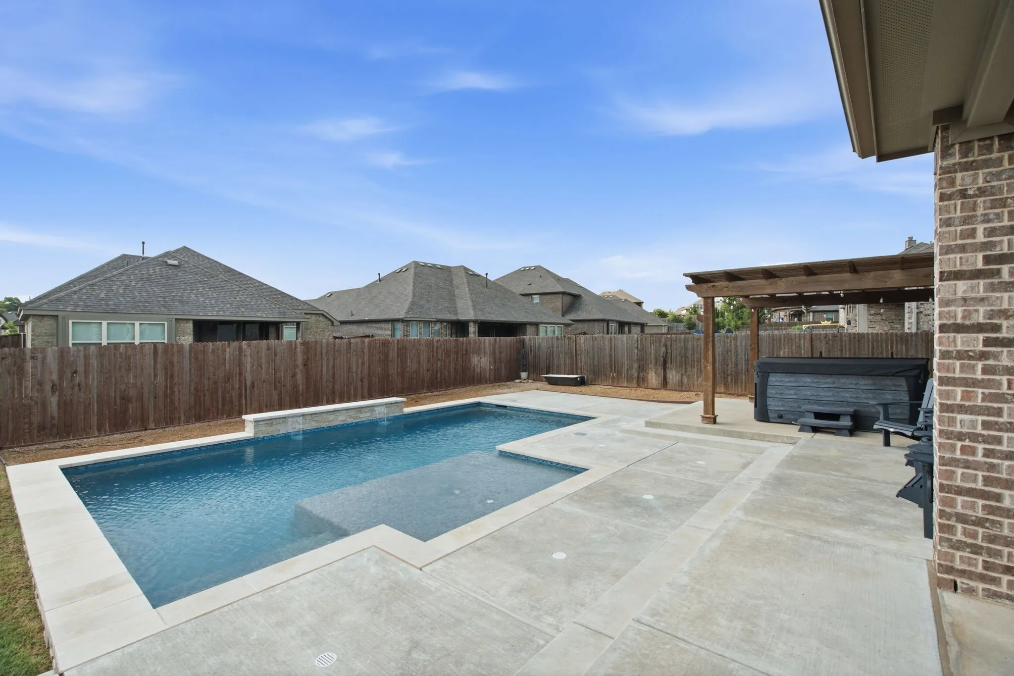 Expansive concrete patio with a rectangular swimming pool, freestanding spa, wood pergola, and brick exterior