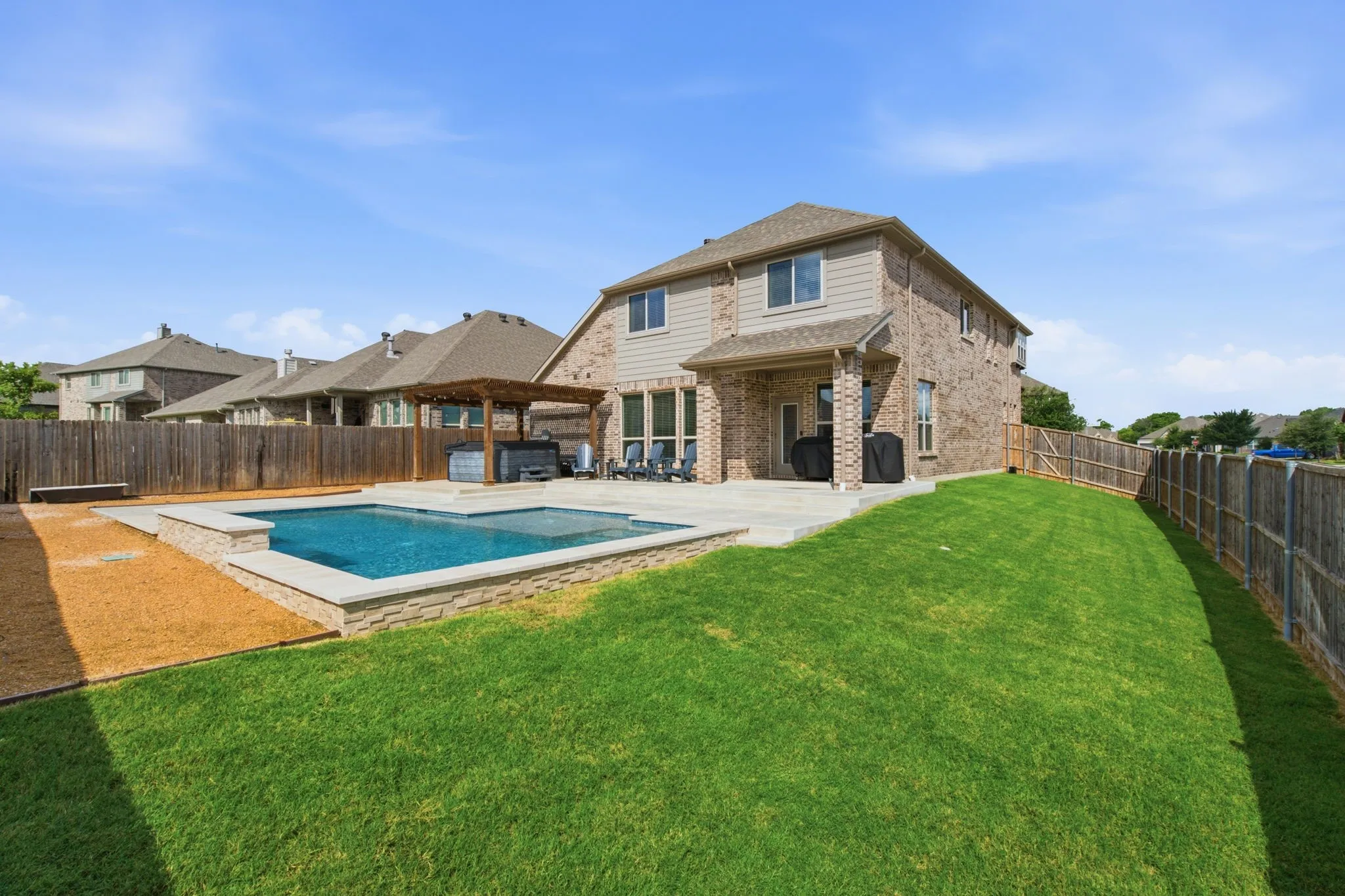 Expansive backyard featuring a rectangular swimming pool with stone coping, a spacious patio area, and a wood pergola and freestanding spa