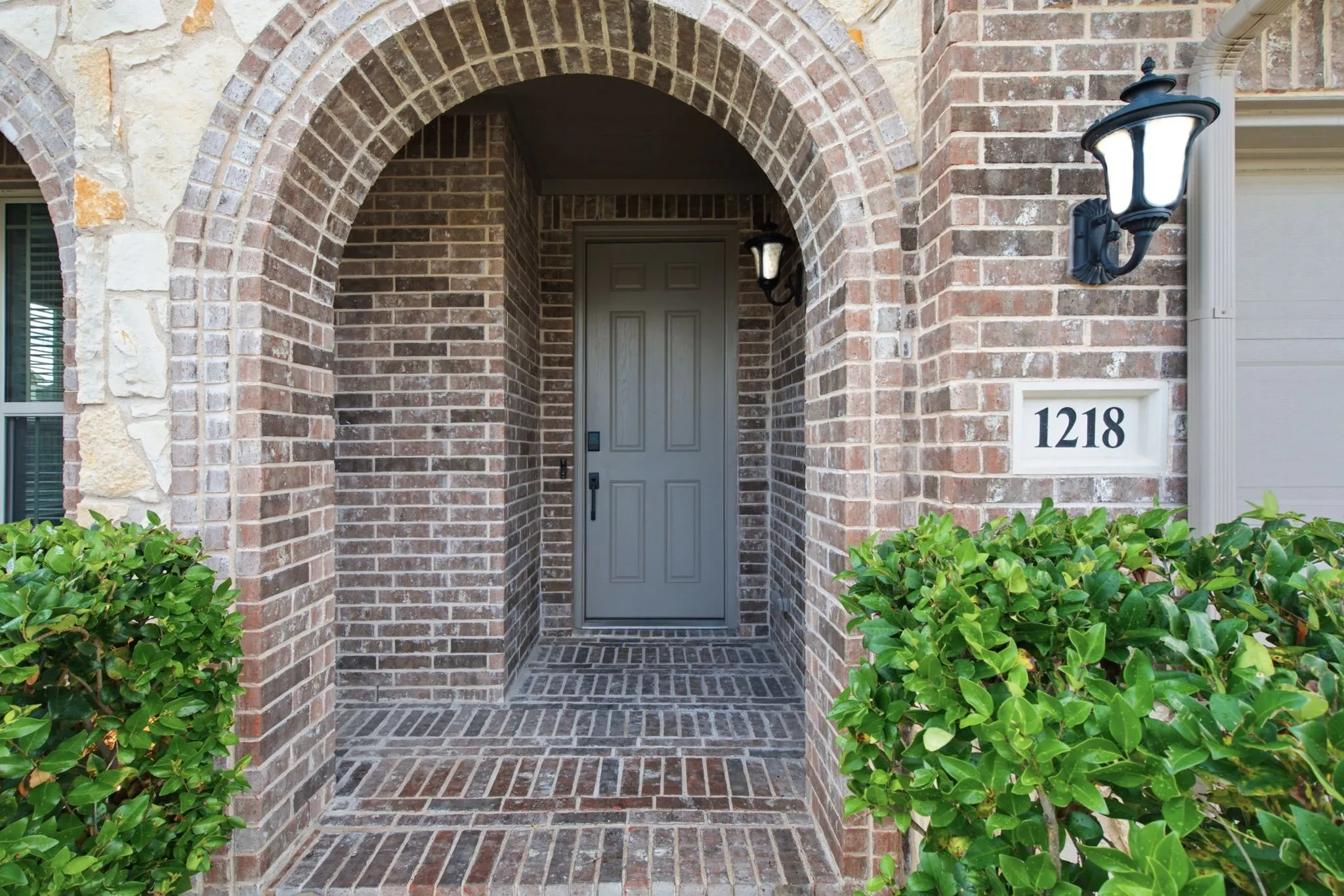 Brick and stone veneer exterior featuring an arched entryway and brick flooring