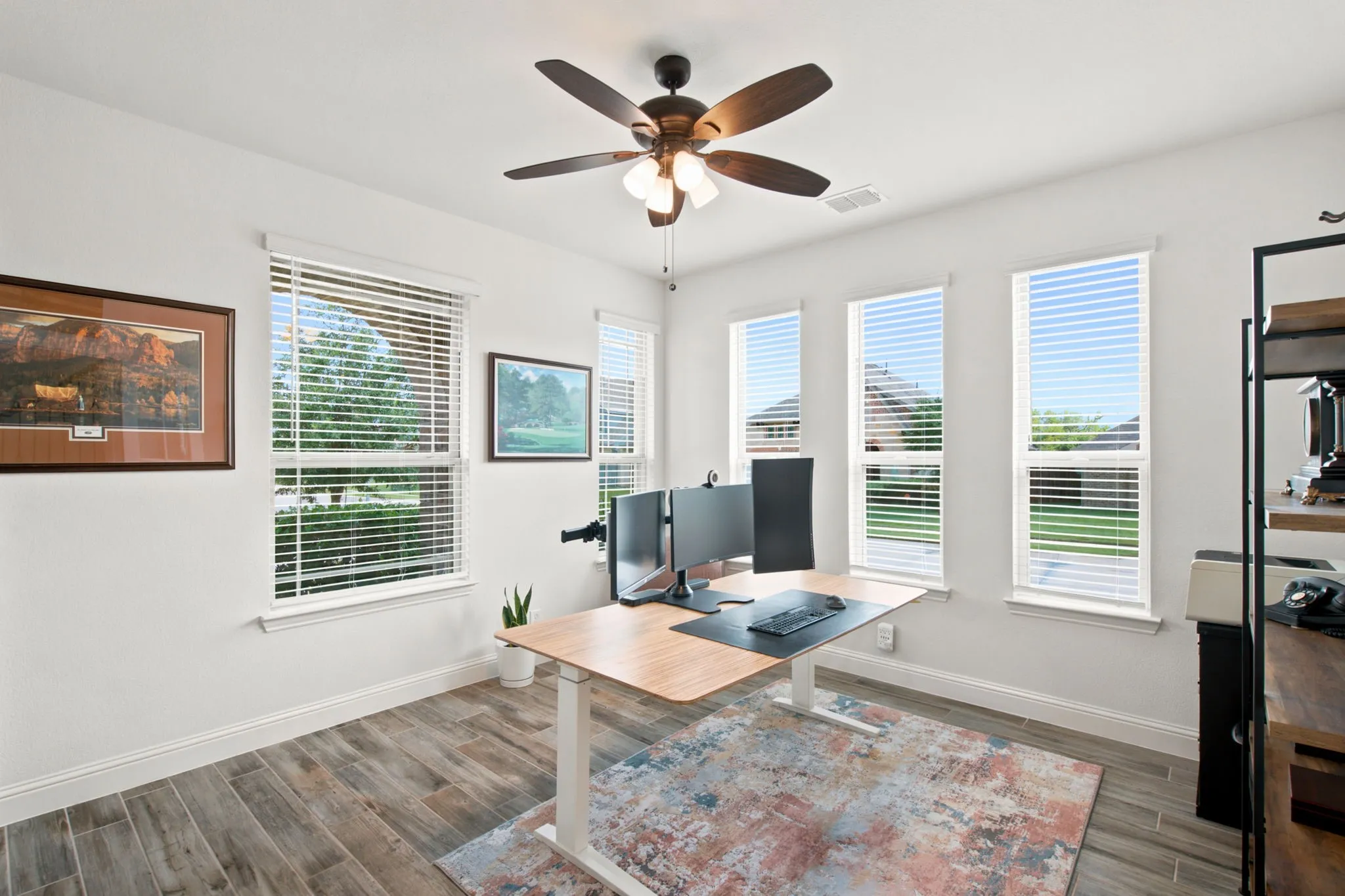Room featuring wood-look tile flooring, multiple windows with blinds, a ceiling fan, and white painted walls