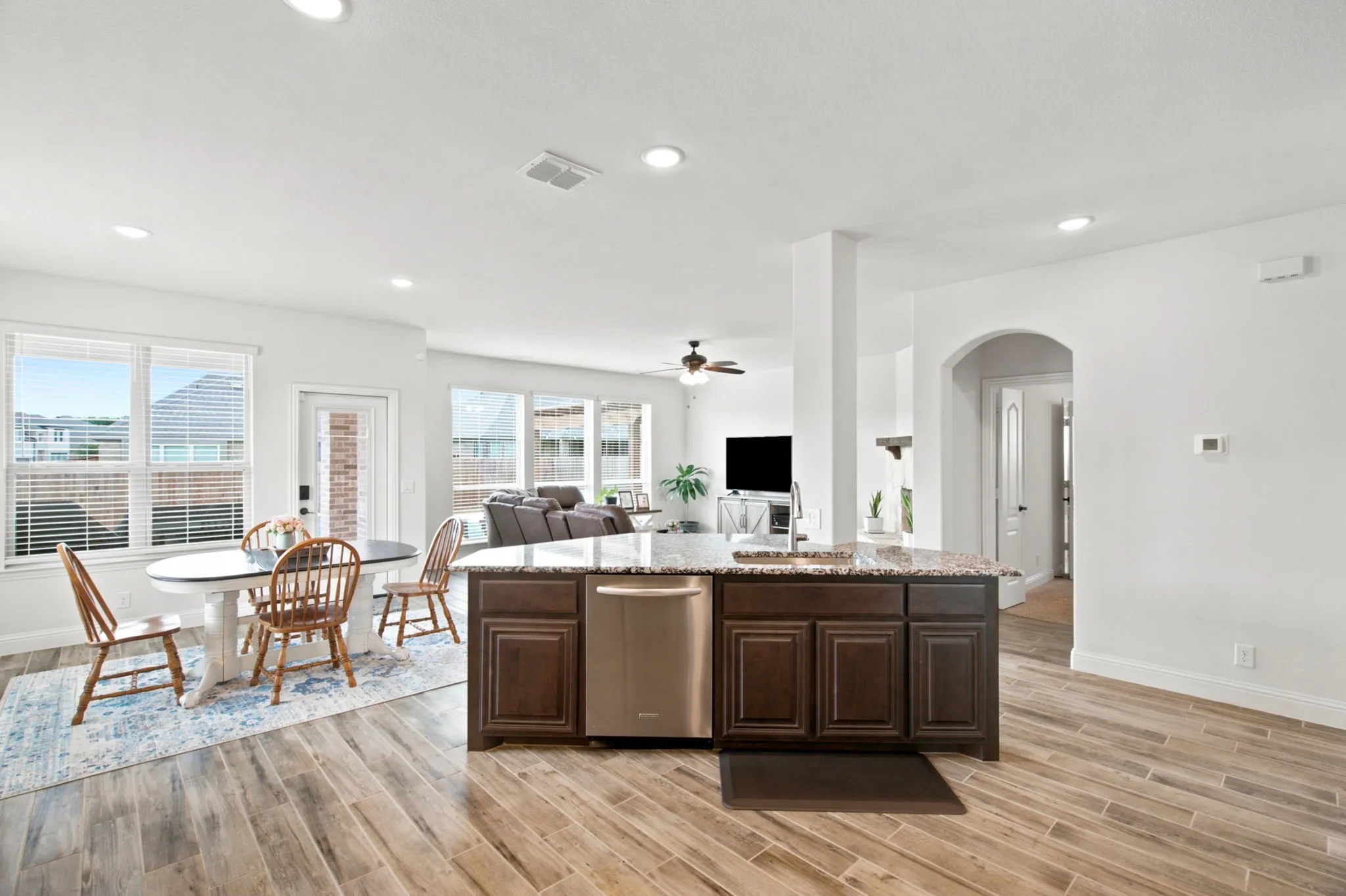 Open-concept kitchen and dining area featuring wood-look tile flooring, recessed lighting, a kitchen island with built-in cabinetry, and stainless steel dishwasher