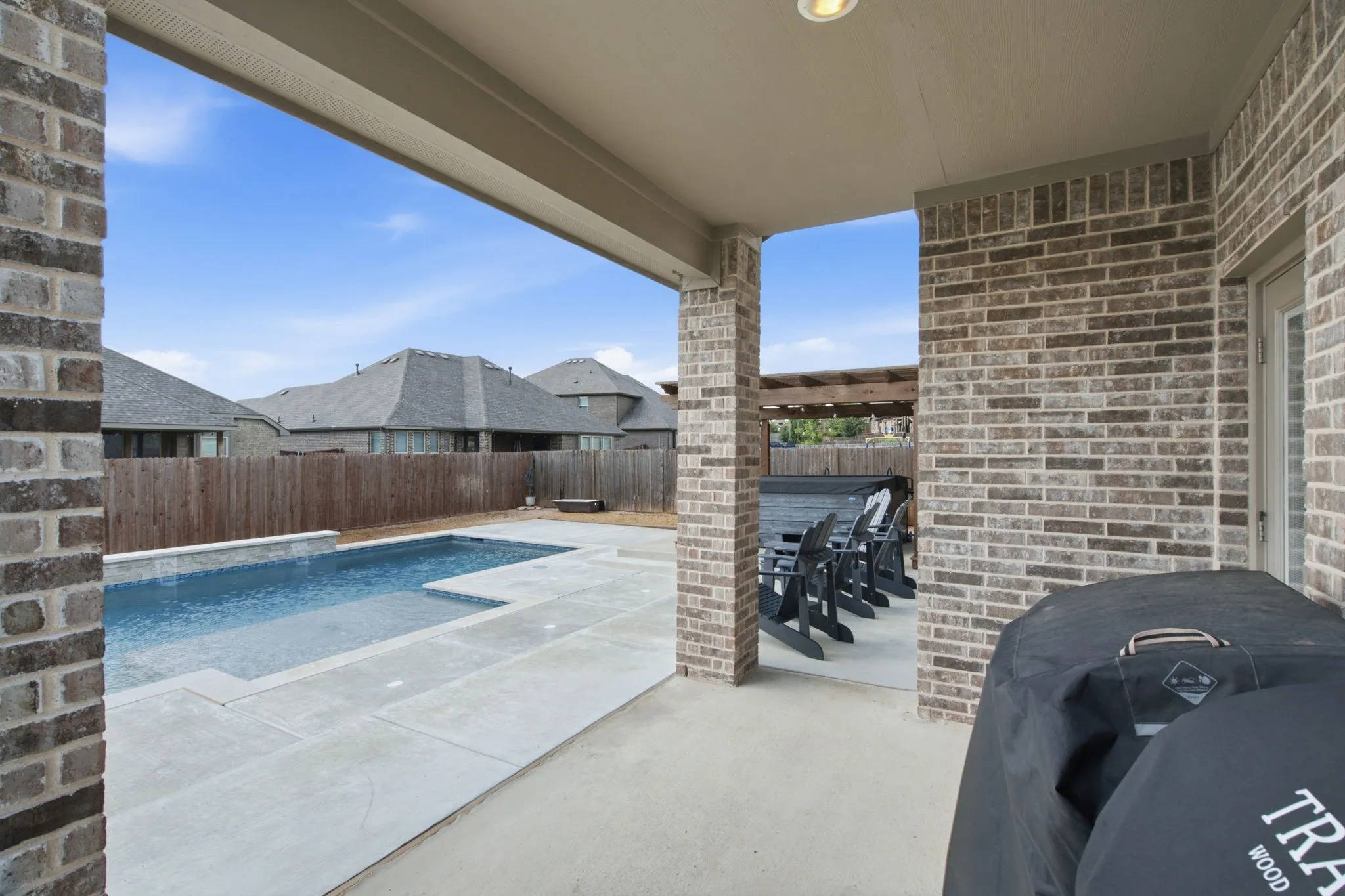 Covered patio area with brick exterior walls, recessed lighting, and an adjacent swimming pool with integrated steps