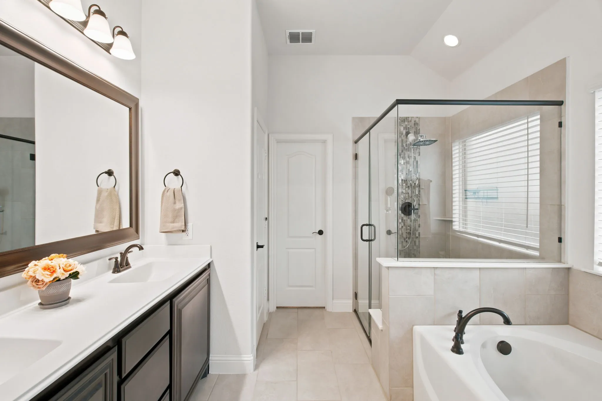 Dual vanity with rectangular sinks, a glass-enclosed shower, a built-in bathtub, and tile flooring
