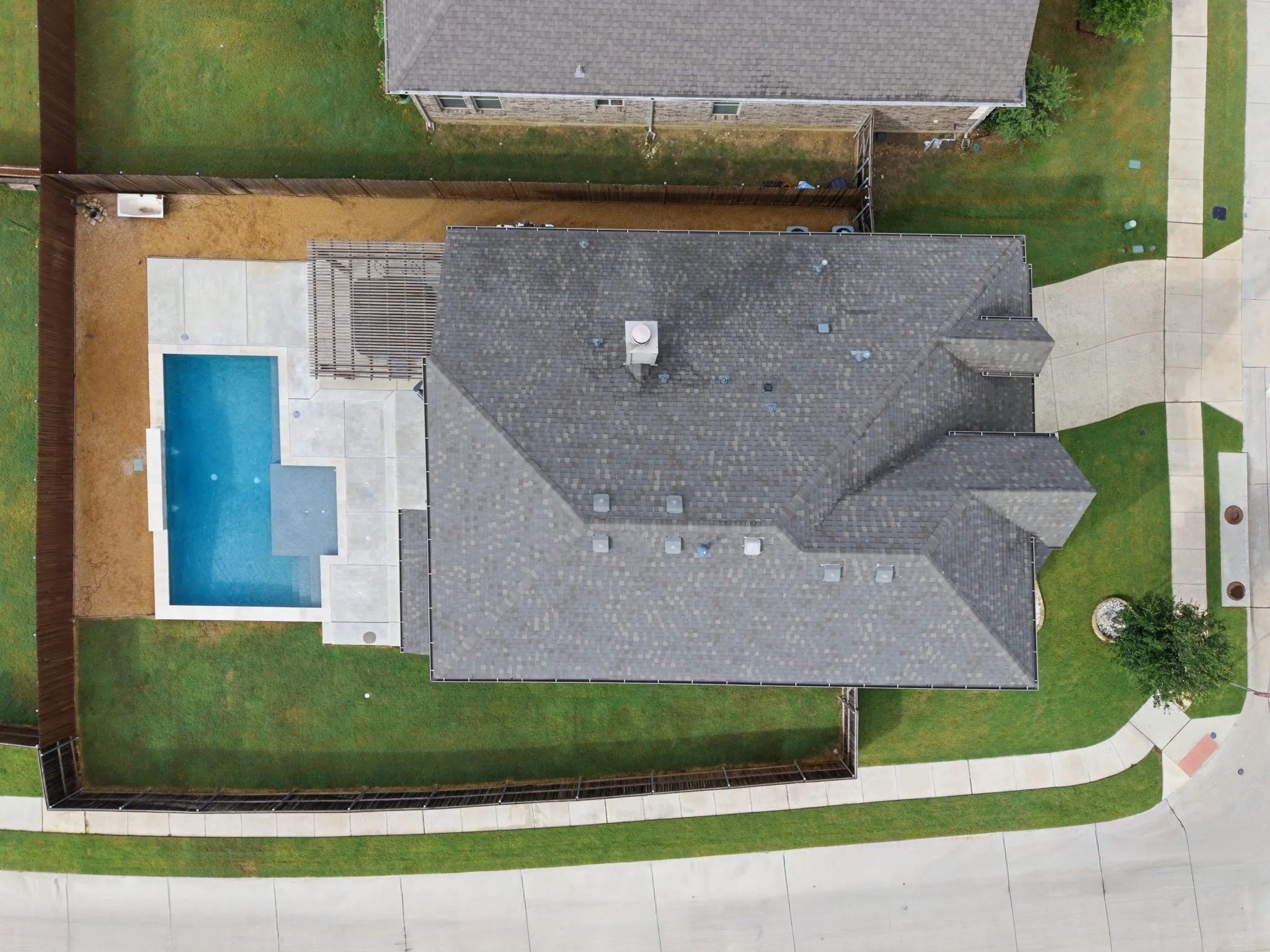 Asphalt shingle roof, concrete patio, in-ground swimming pool, and wood privacy fencing
