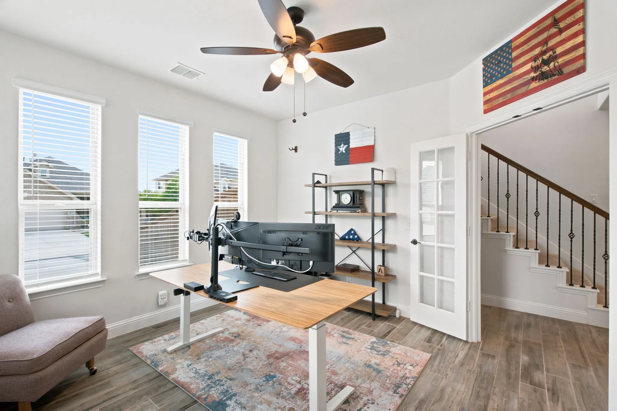 Room featuring three large windows, a ceiling fan with integrated lighting, wood-look tile flooring, and French doors