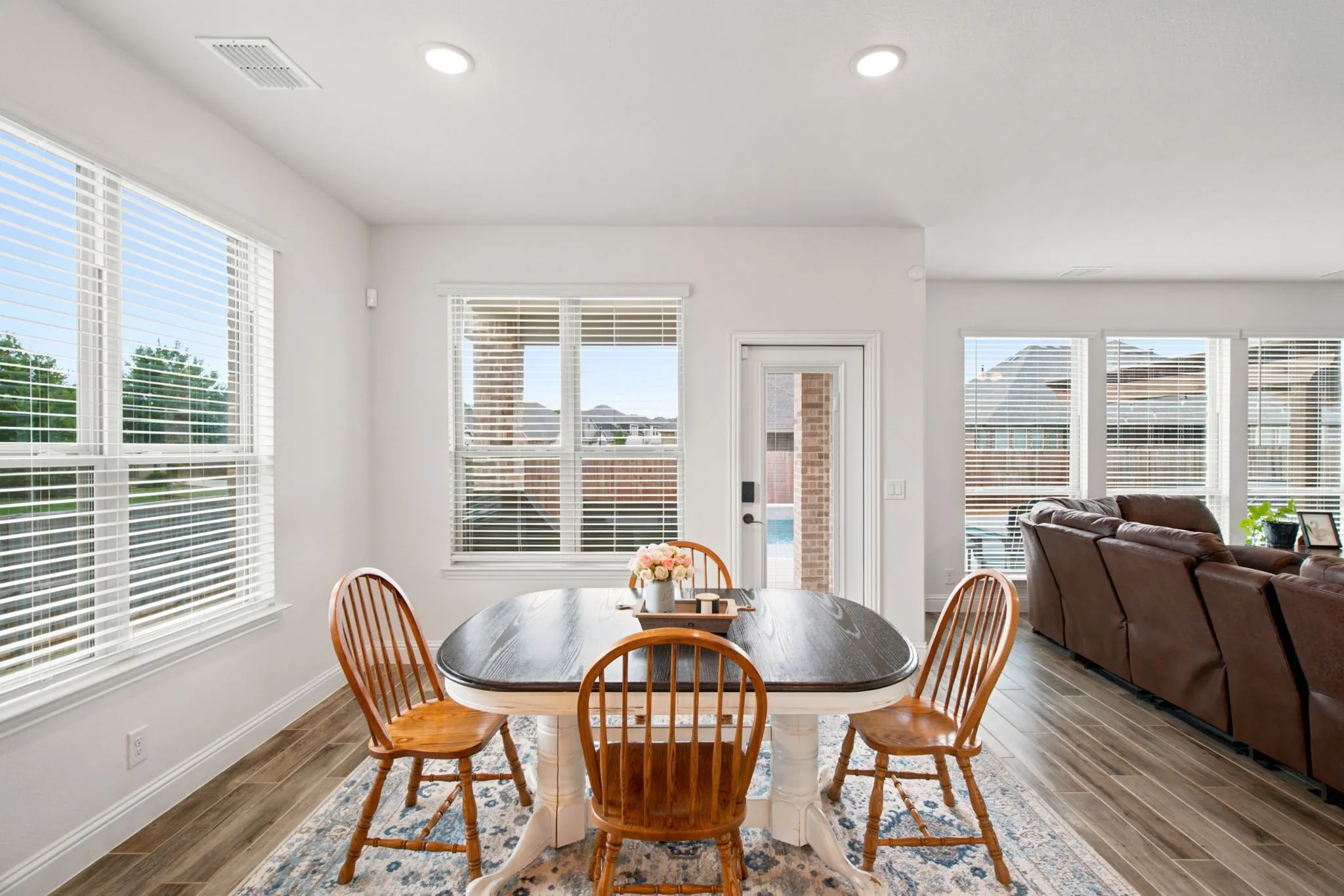 Recessed lighting, multiple windows with blinds, white trim, wood-look tile flooring, and a white door with a clear glass panel