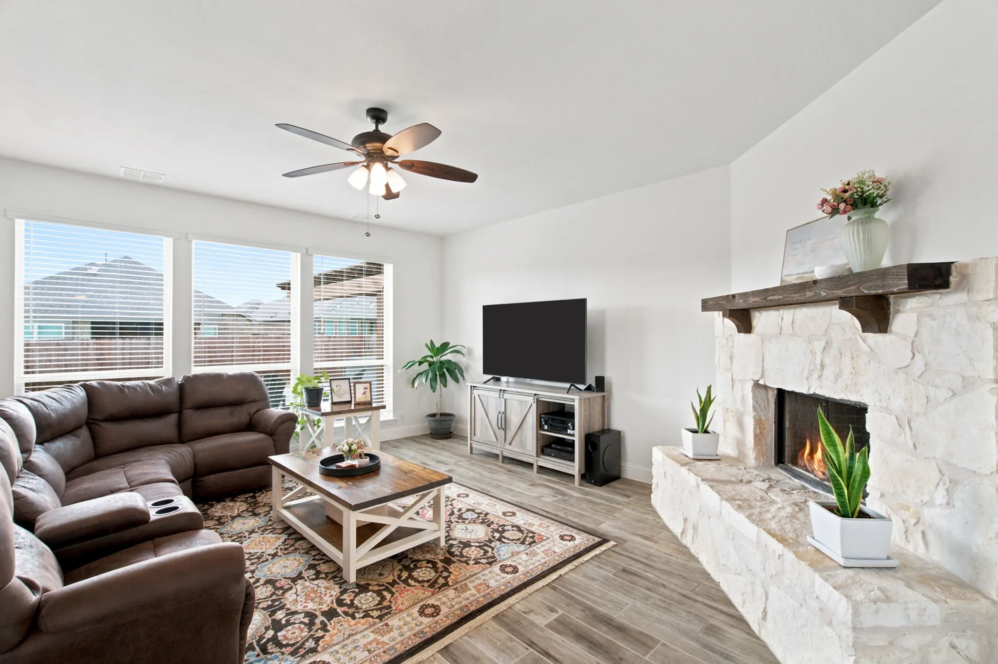 Living area featuring a stone-clad fireplace with a wood mantel, wood-look tile flooring, and multiple windows