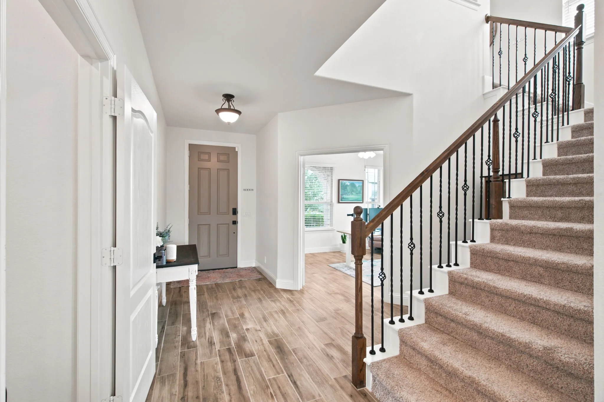 Wood-look tile flooring leading to a staircase with wrought iron balusters and a wood handrail
