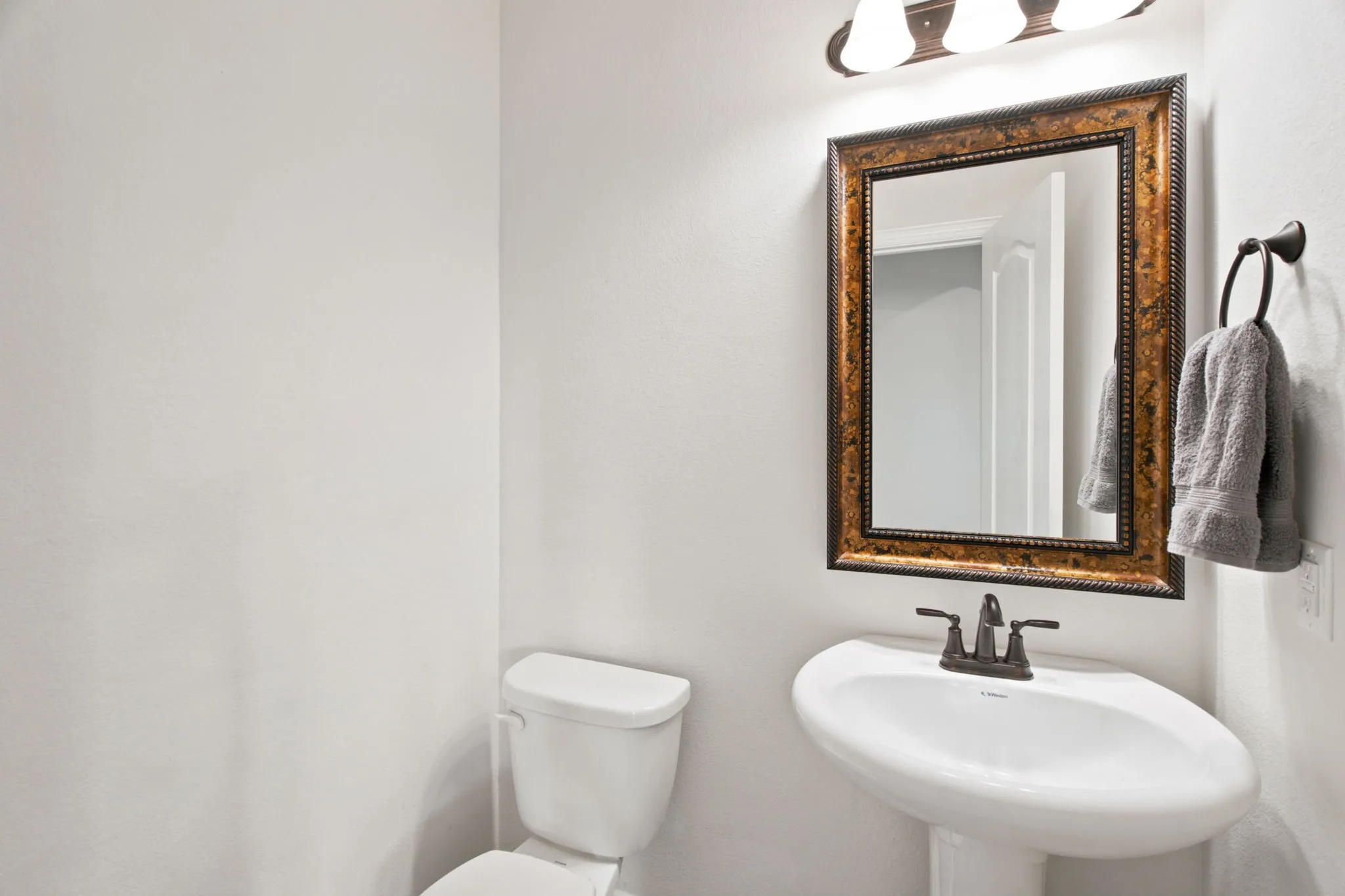 Pedestal sink with dark bronze faucet, framed mirror with ornate detailing, and wall-mounted lighting