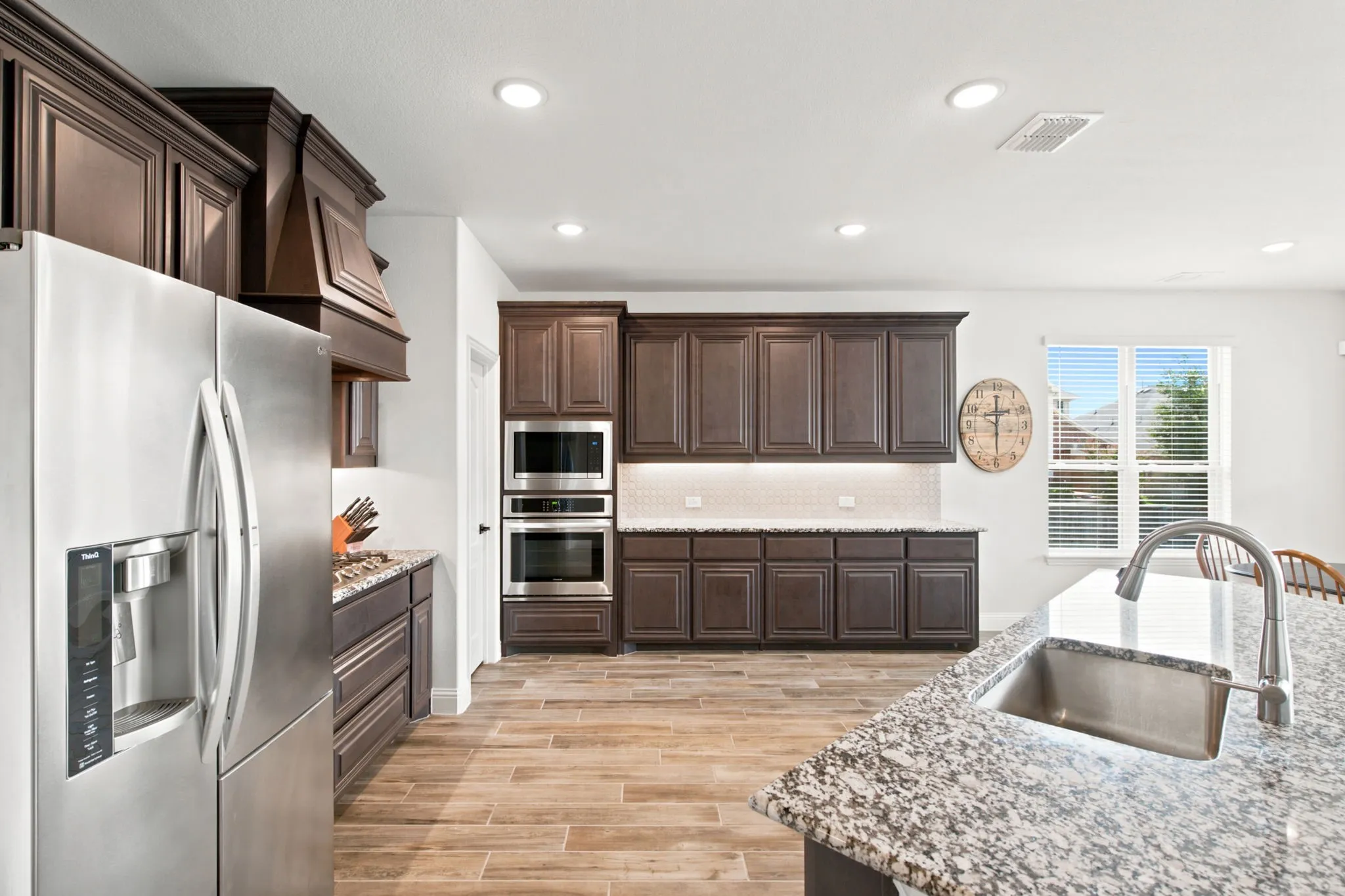 Gourmet kitchen featuring wood-look tile flooring, dark wood cabinetry, stainless steel appliances, speckled stone countertops, and recessed lighting
