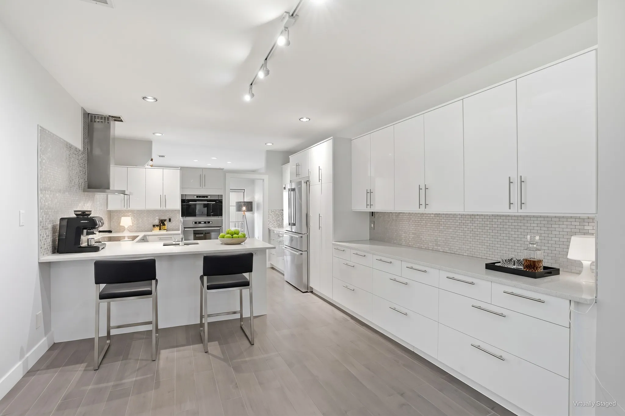 Kitchen with breakfast bar seating, built-in wall oven, stainless appliances, and tall pantry cabinetry. Virtually staged.