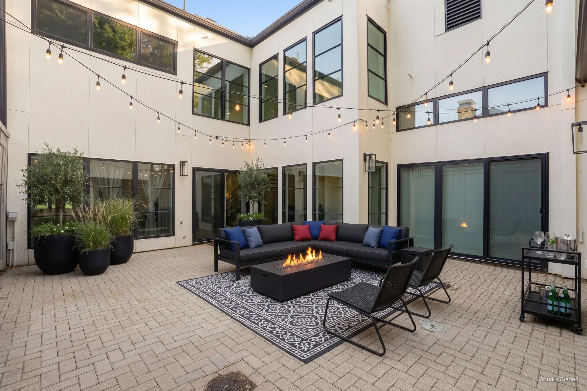 Private herringbone brick courtyard at the center of the home, framed by two stories of black-framed glass. Virtually staged.