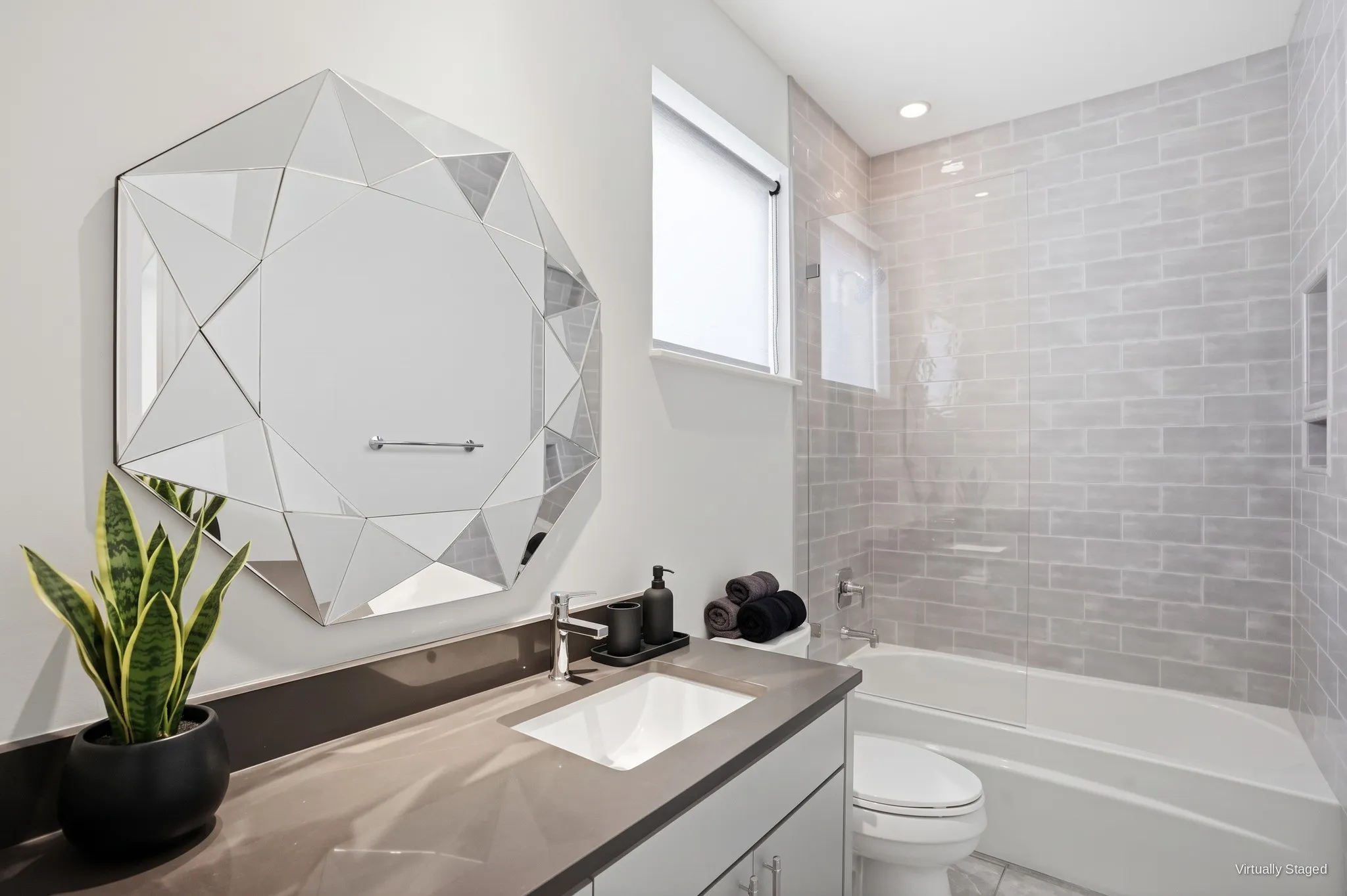 Full bath with quartz vanity, tub and shower combo with glass panel, and gray tile surround with a built-in niche. Virtually staged.
