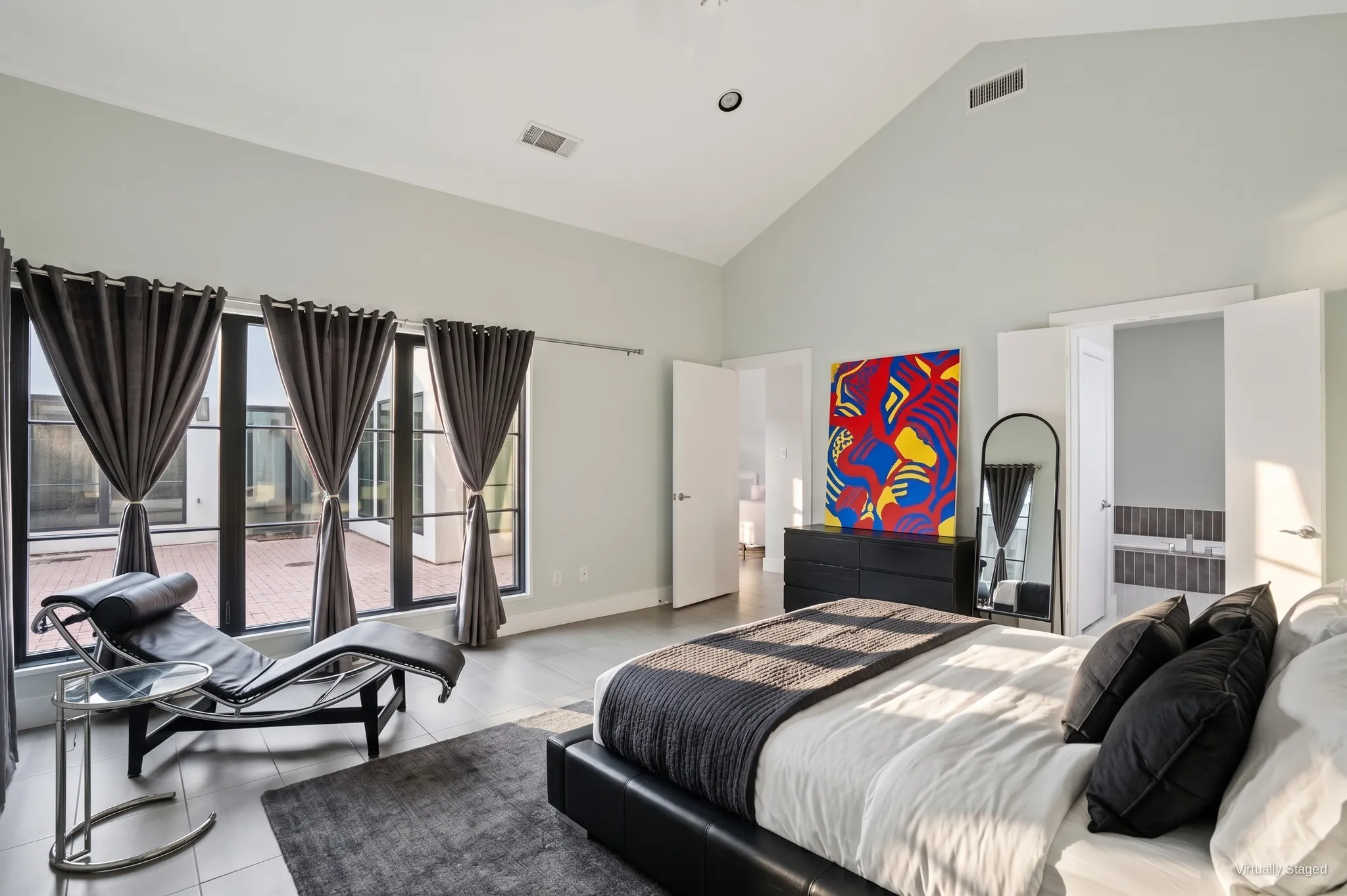 Primary bedroom with double doors to the ensuite bath and natural light from the courtyard windows. Virtually staged.