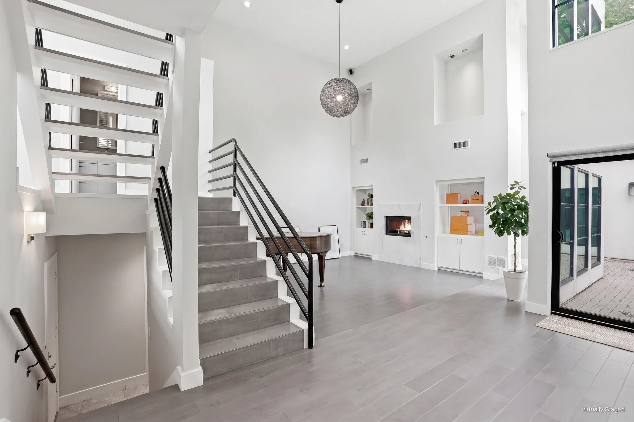 Great room with soaring two-story ceilings, a marble gas fireplace flanked by built-in shelving, and an open staircase to the upper levels. Virtually staged.
