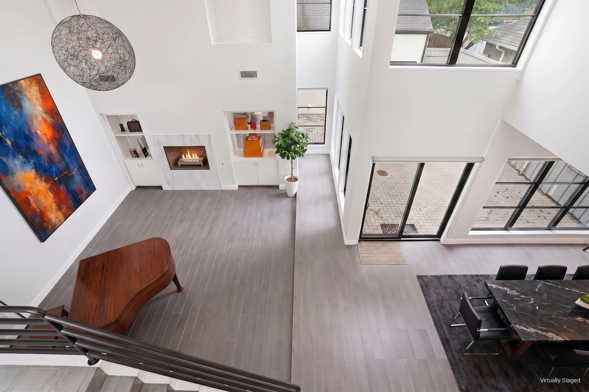 Overhead view of the two-story great room and open floor plan, with floor-to-ceiling glass doors to the courtyard. Virtually staged.