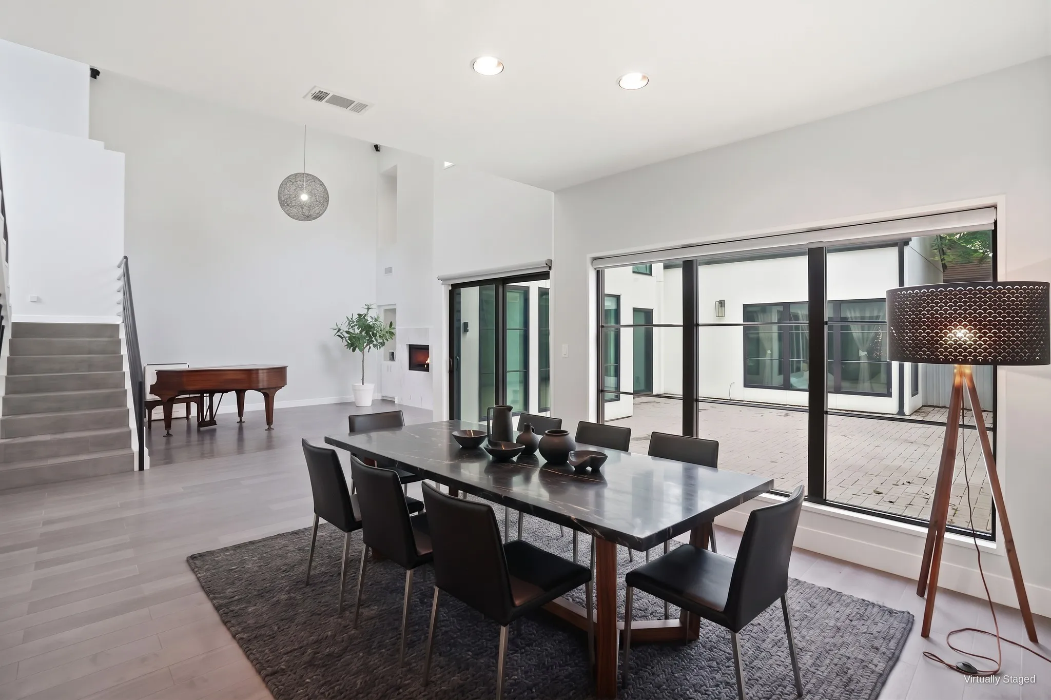 Open dining and living space with a wall of black-framed glass looking out to the private courtyard. Virtually staged.