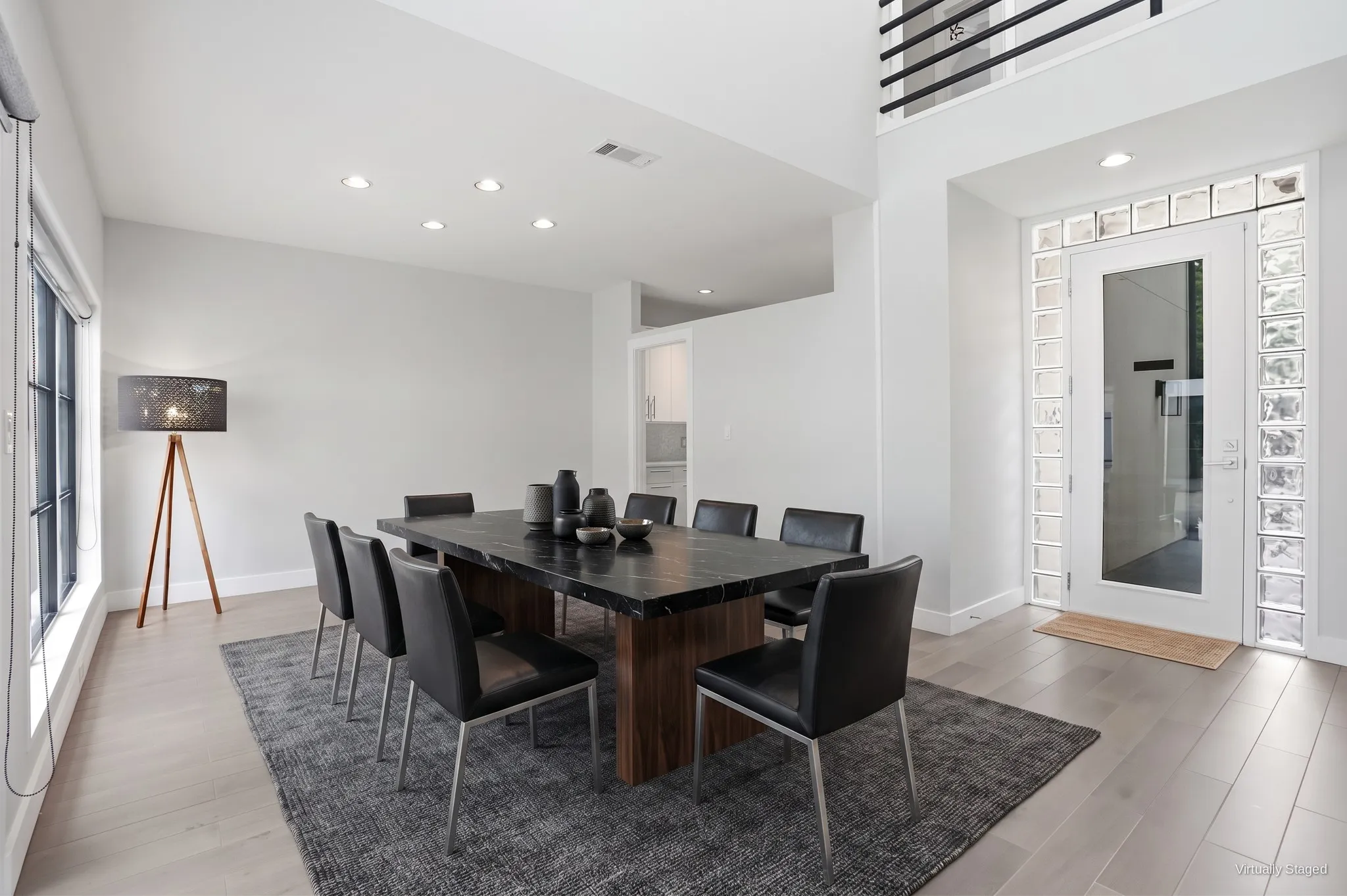 Dining room just inside the front entry, with recessed lighting and tall black-framed windows along the courtyard side. Virtually staged.