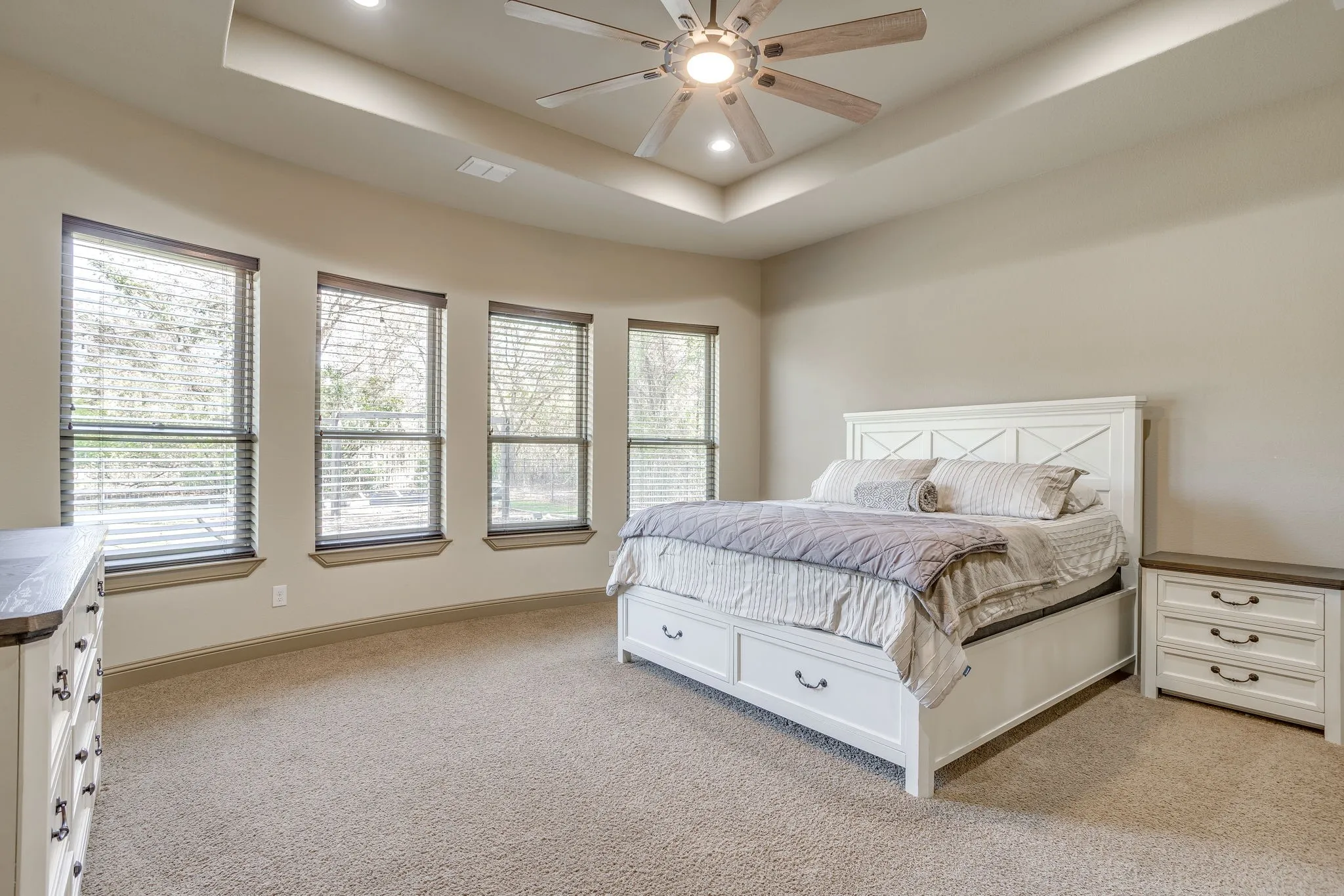 The spacious primary bedroom with a wall of windows overlooking the backyard, room for a sitting area and tray ceiling.