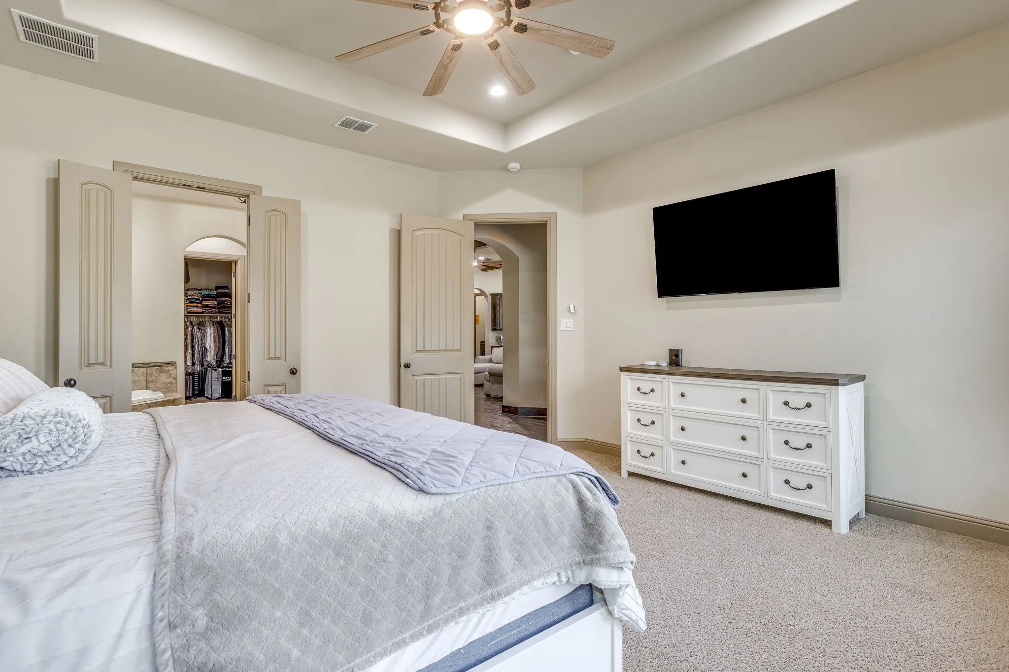 The spacious primary bedroom with a wall of windows overlooking the backyard, room for a sitting area and tray ceiling.
