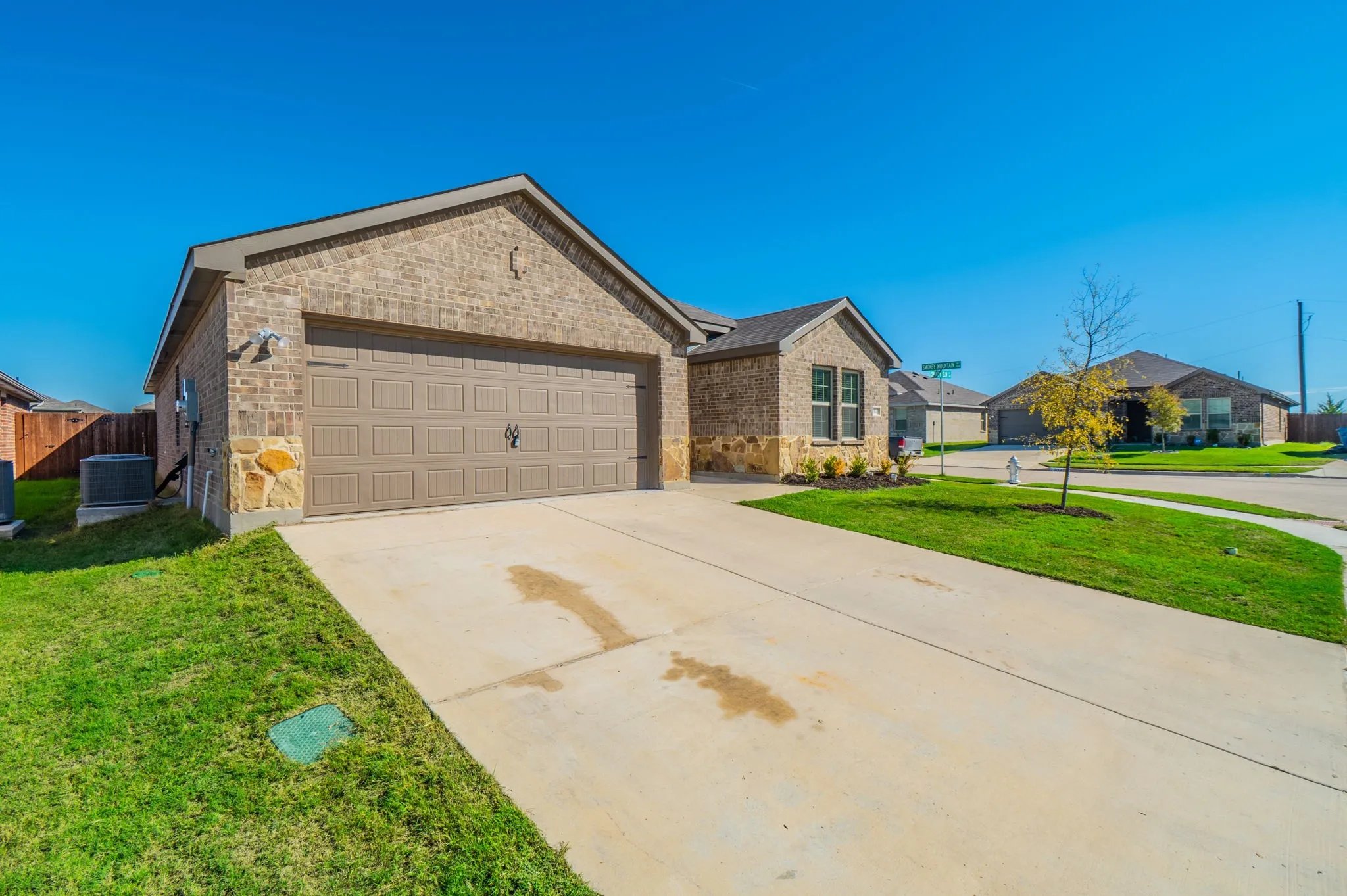 Brick exterior with stone accents, attached two-car garage, concrete driveway, and front lawn