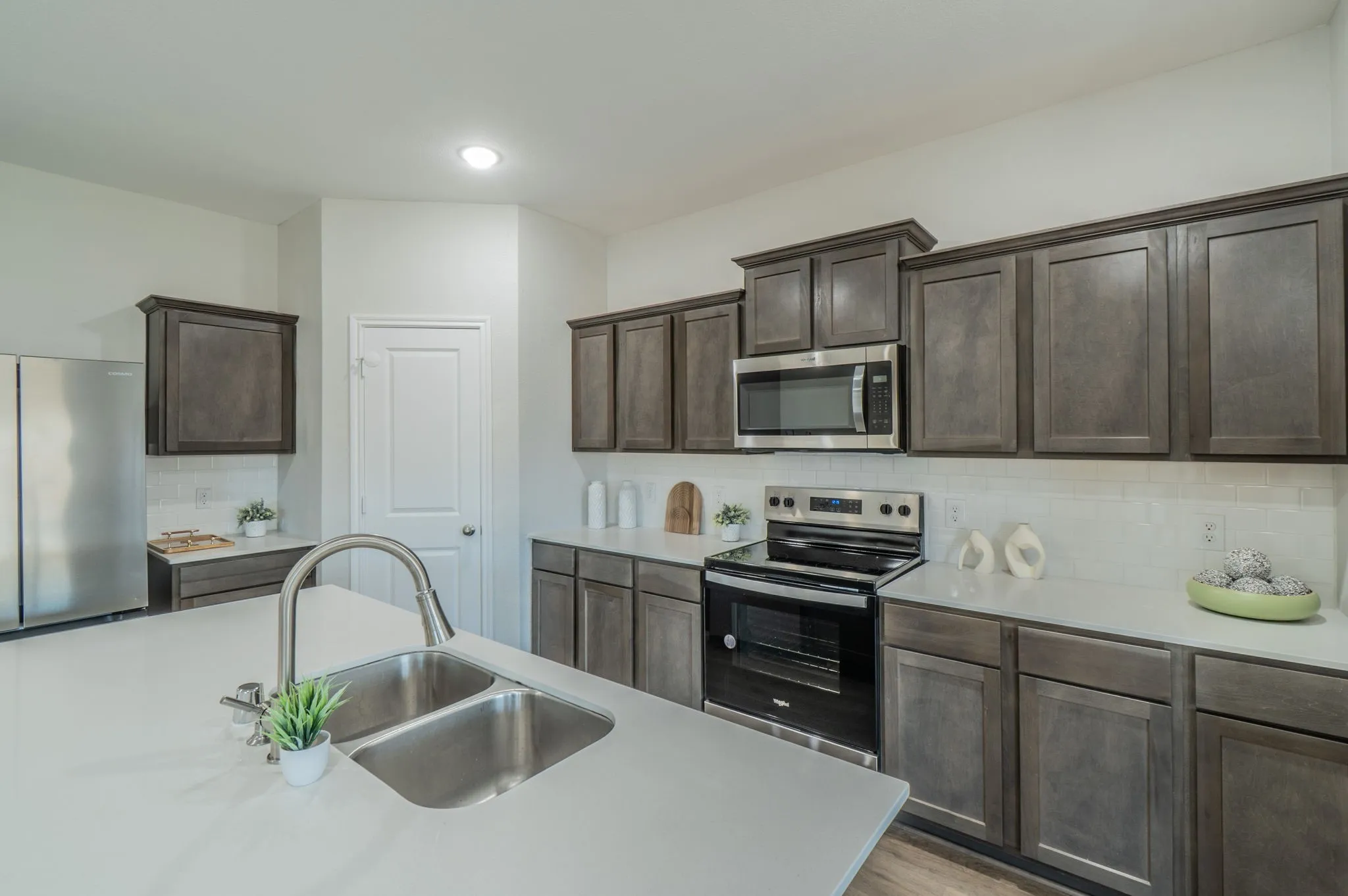 Kitchen featuring a stainless steel double basin sink, brushed nickel faucet, light-toned countertops, and dark wood-finish cabinetry