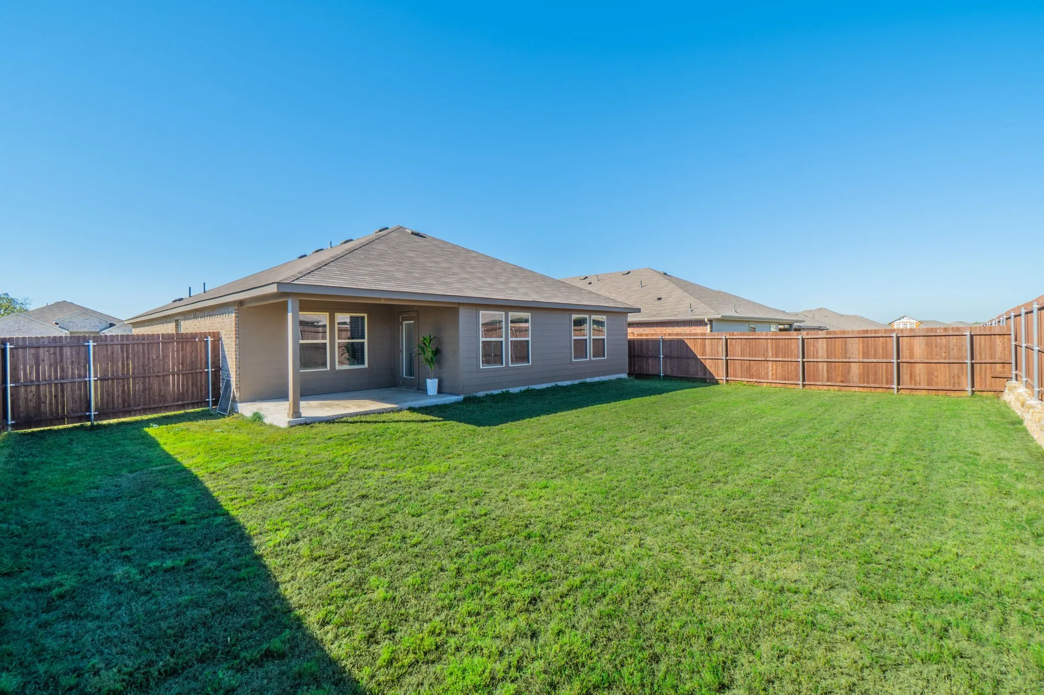 Expansive backyard featuring a manicured lawn, full privacy fencing, and a covered patio area