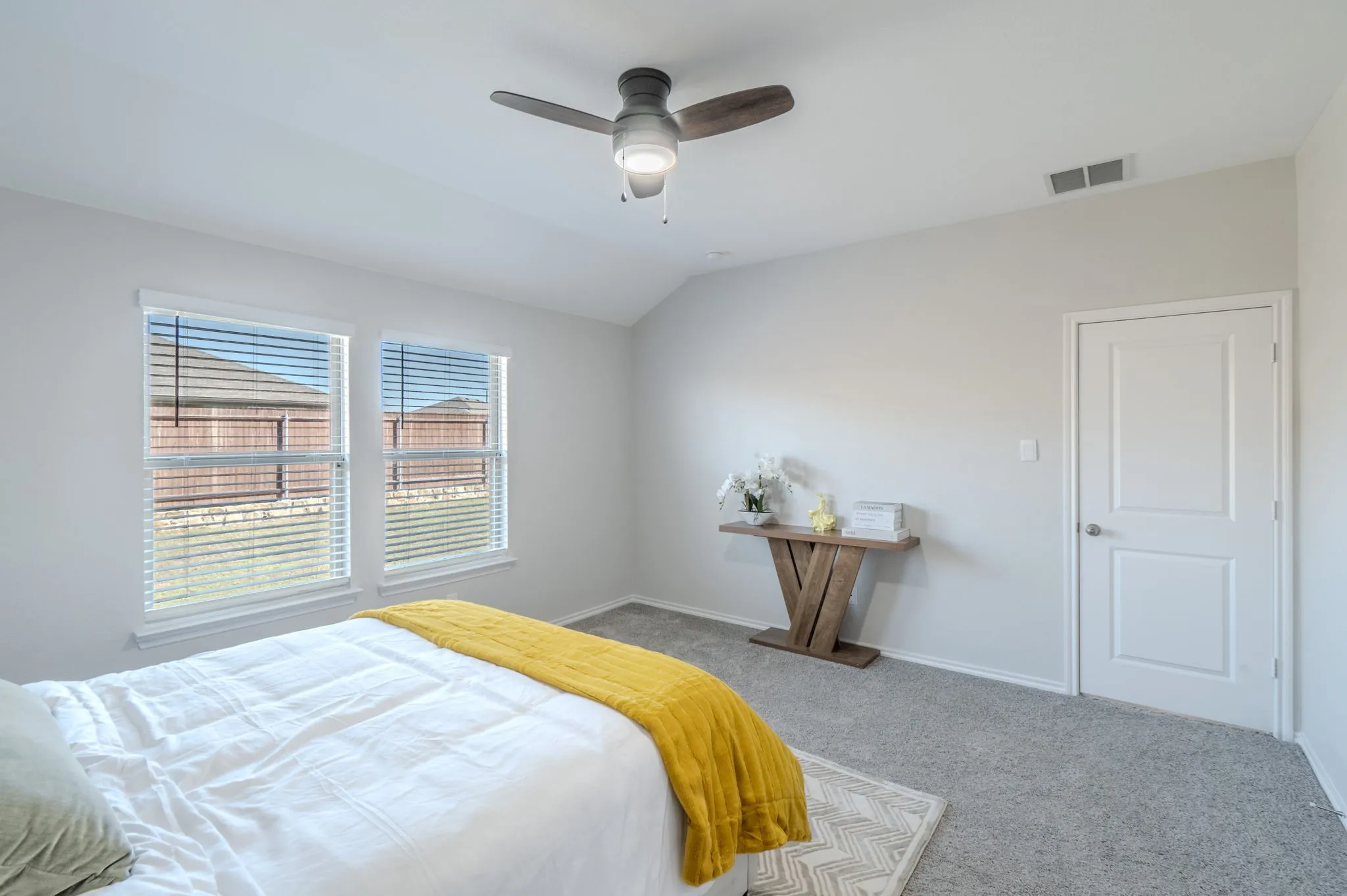 Vaulted ceiling with a contemporary ceiling fan, two double-hung windows with blinds, light gray wall paint, and gray carpeting