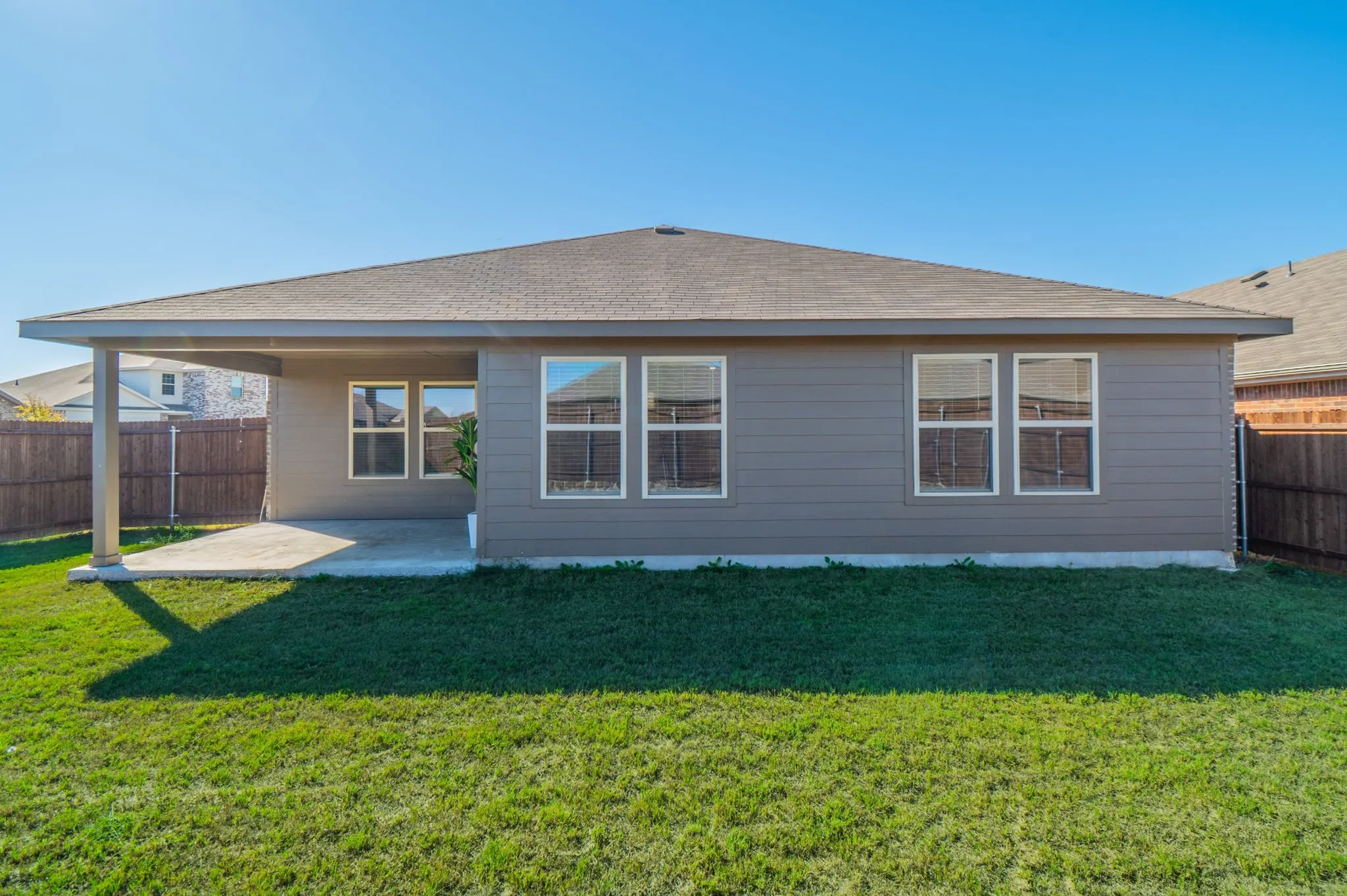 Rear exterior featuring a covered patio, multiple windows, and a fenced perimeter