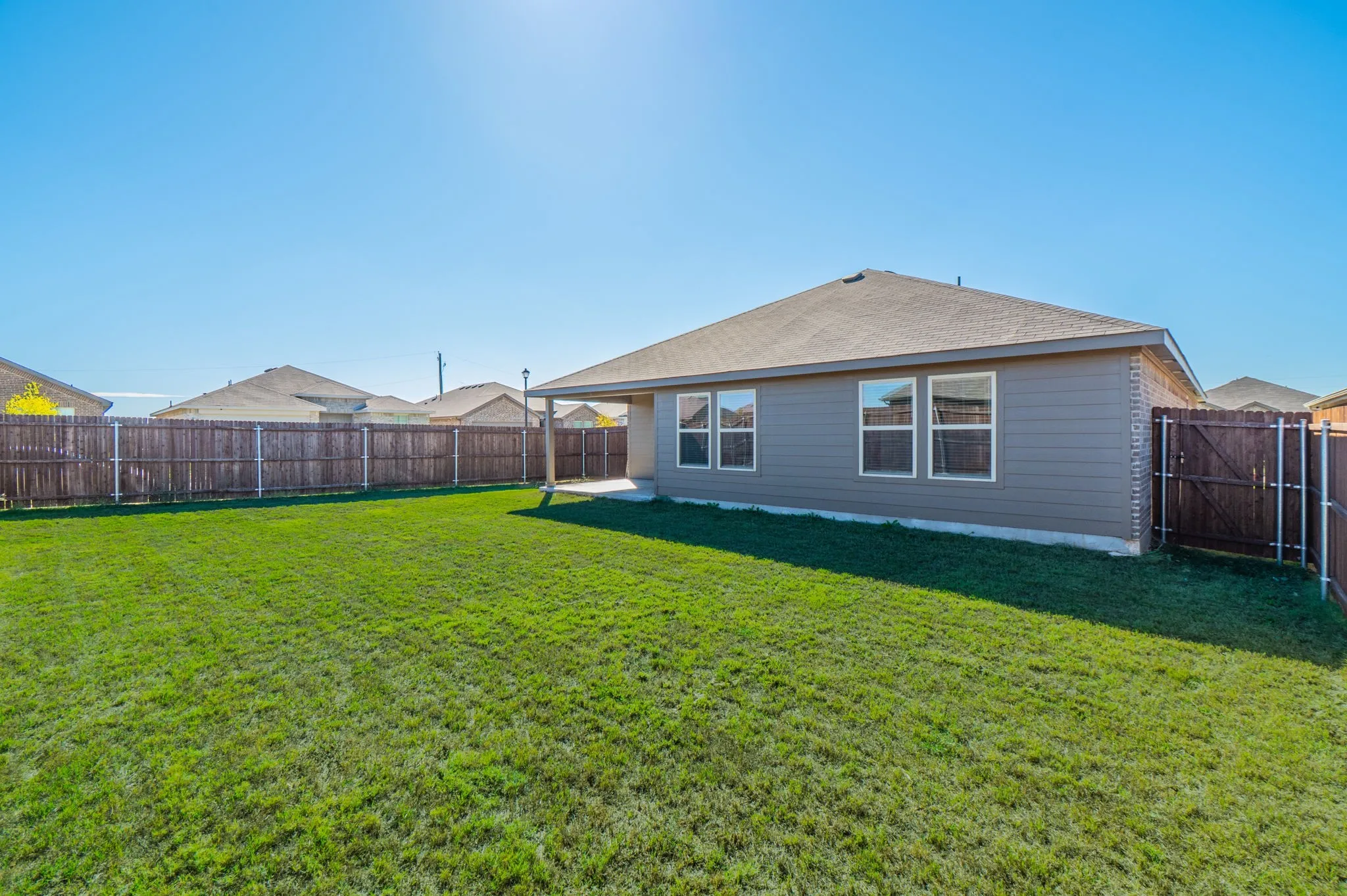 Expansive green lawn, wood fence, concrete patio, and exterior siding