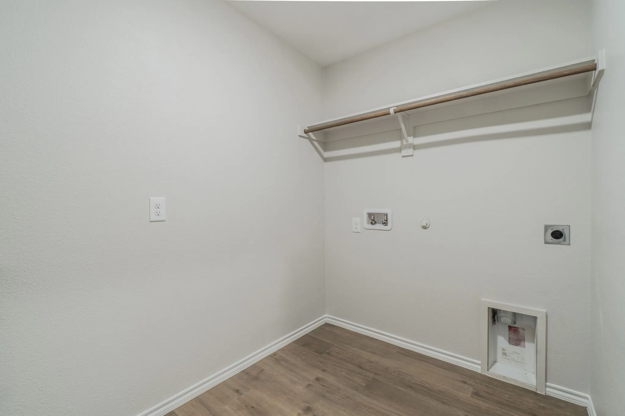 Laundry area featuring wood-finish flooring, a wall-mounted shelving unit with a hanging rod, and utility hookups