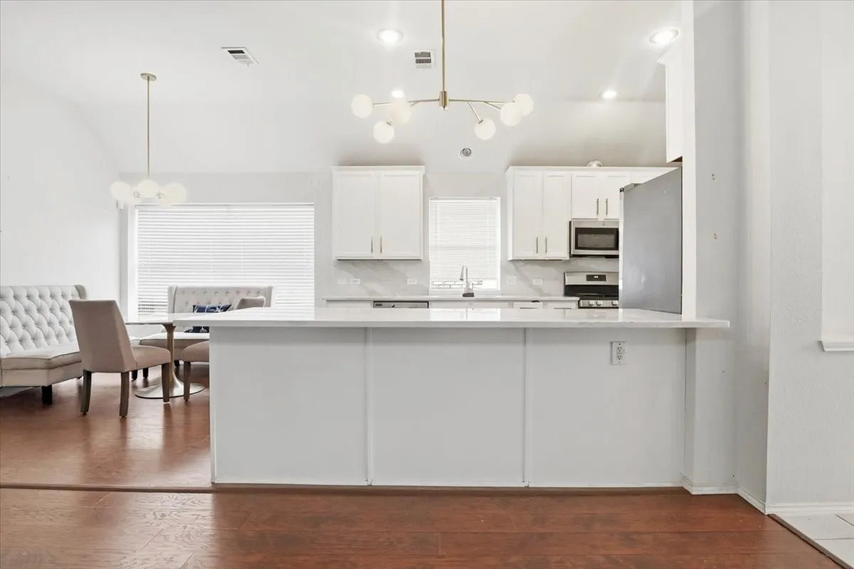 Open-concept kitchen featuring white cabinetry, stainless steel appliances, a white island, and wood-finish flooring