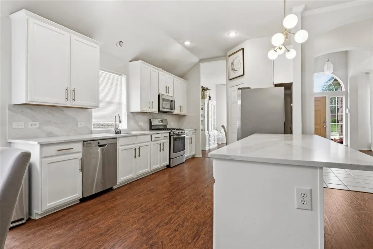 Kitchen with white cabinetry, stainless steel appliances, marble-patterned countertops, wood-finish flooring, and a contemporary chandelier