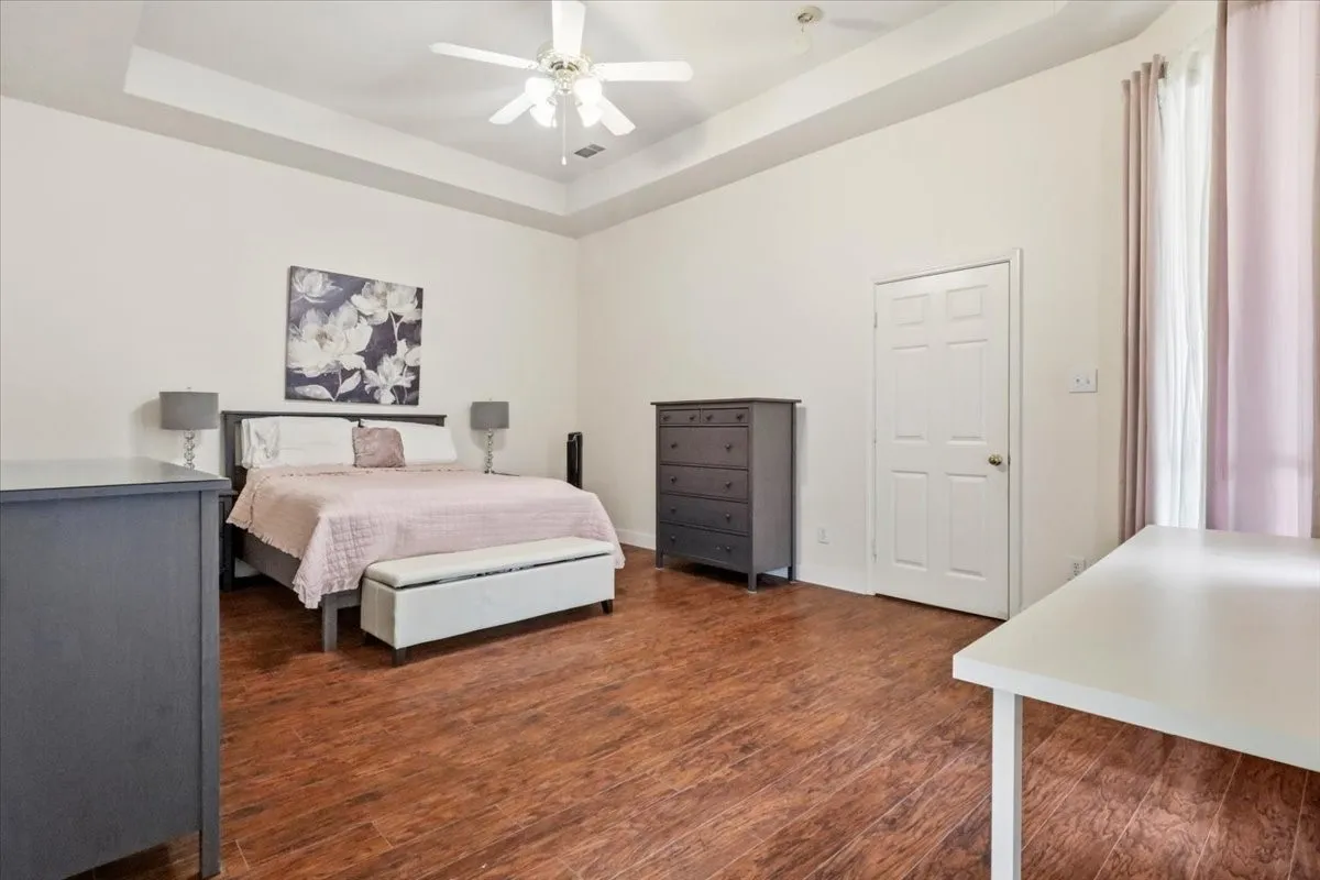 Tray ceiling with a ceiling fan, wood-finish flooring, and white trim throughout