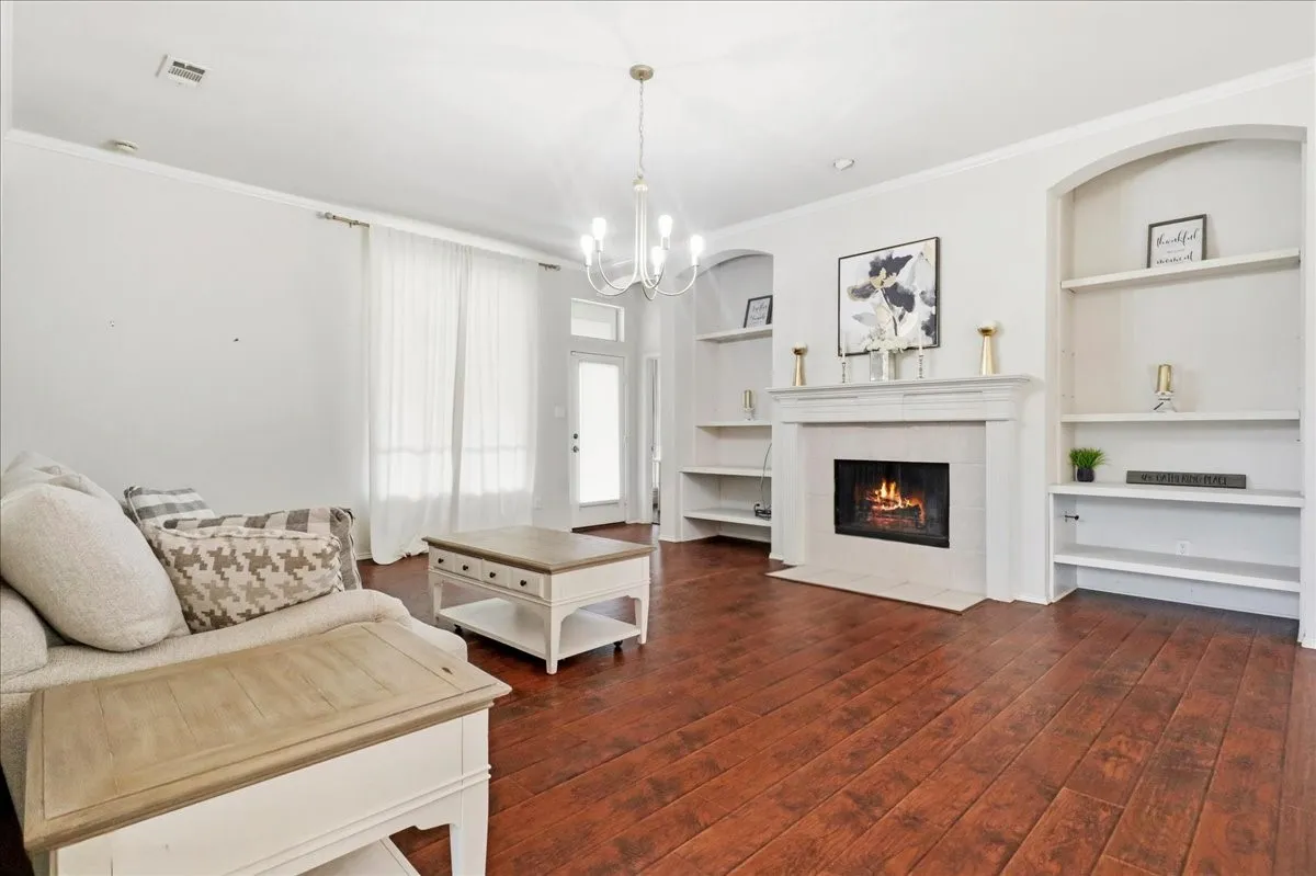 Wood-finish flooring, built-in shelving, a fireplace with a mantel, crown molding, and a chandelier