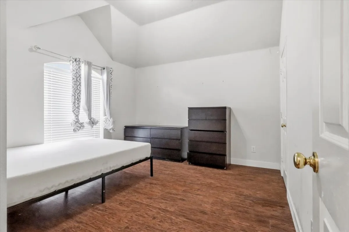 Vaulted ceiling, wood-finish flooring, white paneled door with brass hardware, window with blinds