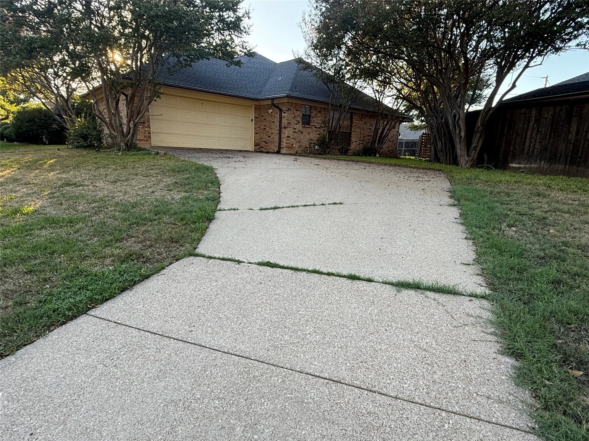Brick exterior with a prominent two-car garage, concrete driveway, and mature trees