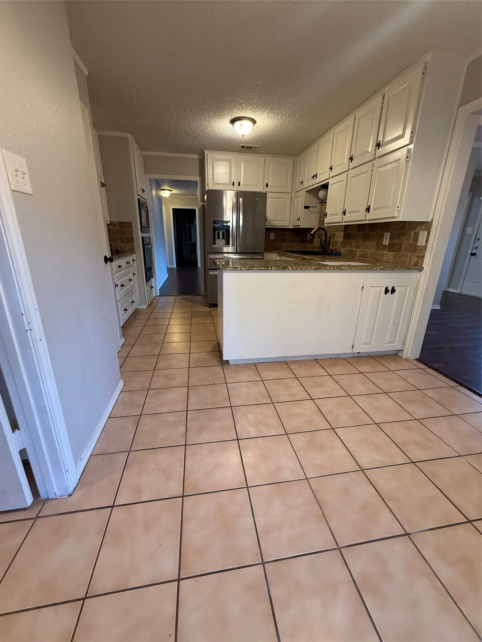 Ceramic tile flooring, white cabinetry, stainless steel refrigerator, built-in ovens, and a tiled backsplash