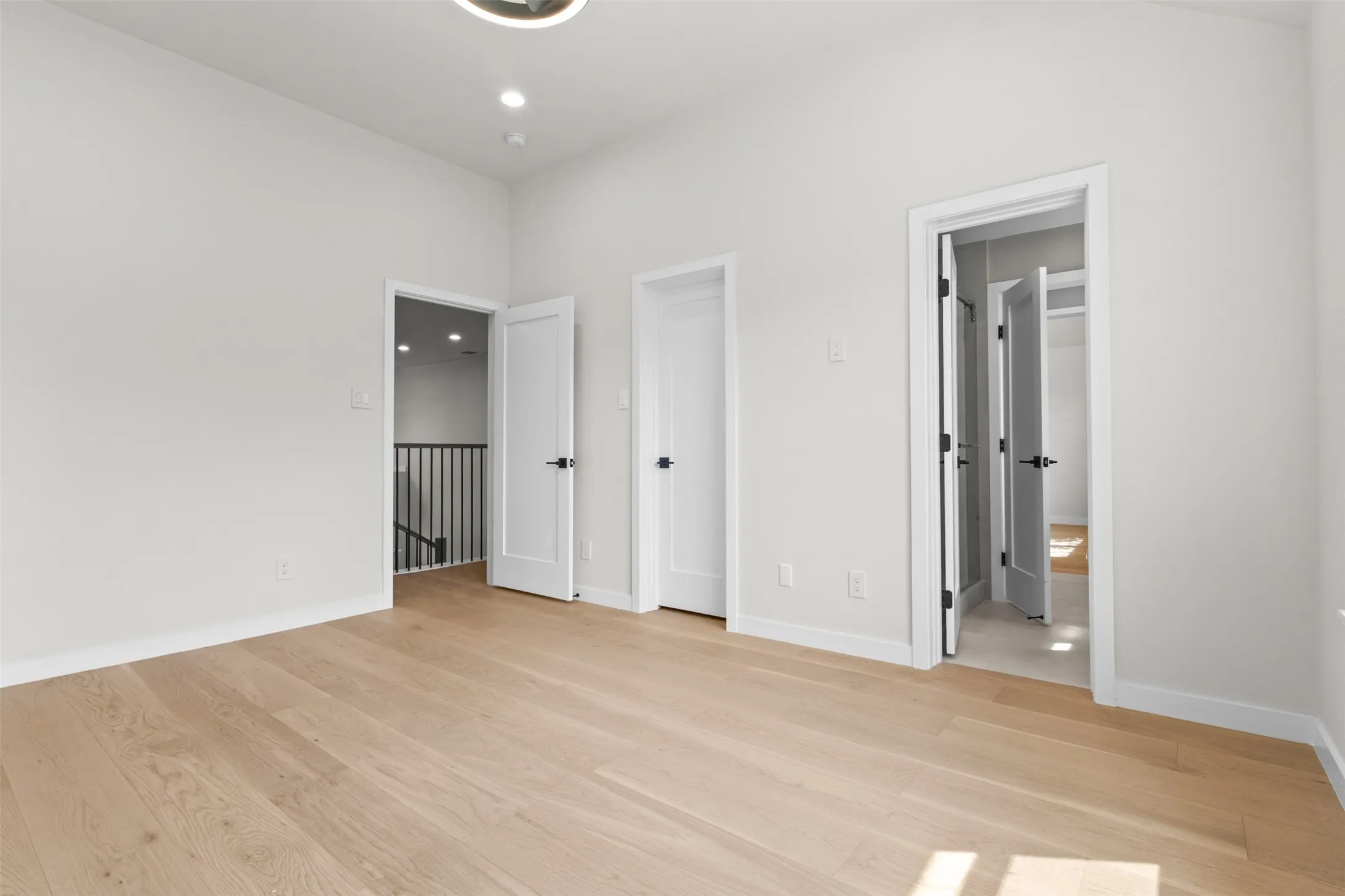 Light-toned wood-finish flooring, recessed ceiling lighting, and multiple white panel doors with matte black hardware