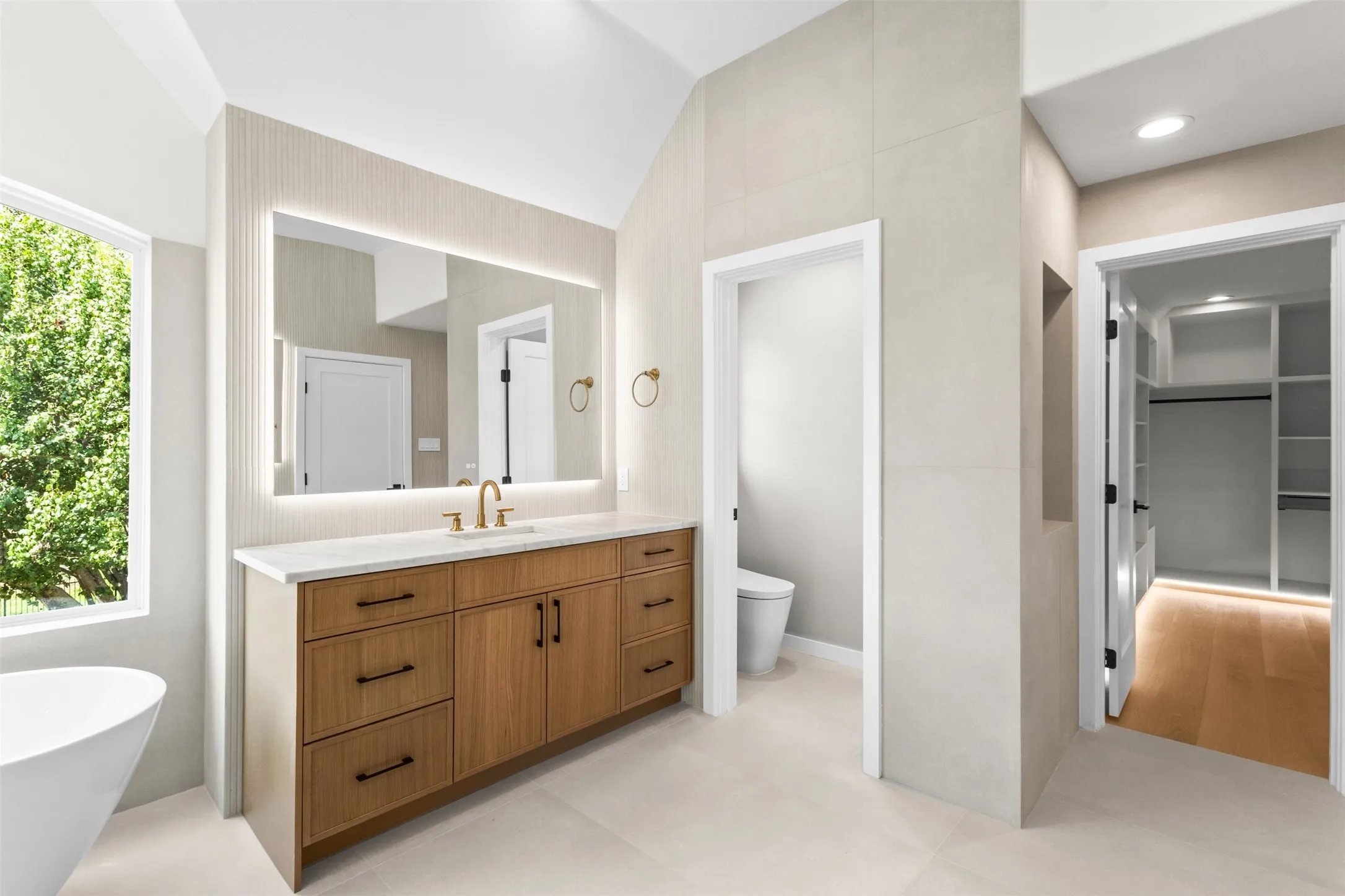 Wood-finish dual vanity with quartz countertop, back-lit mirror, and brass fixtures