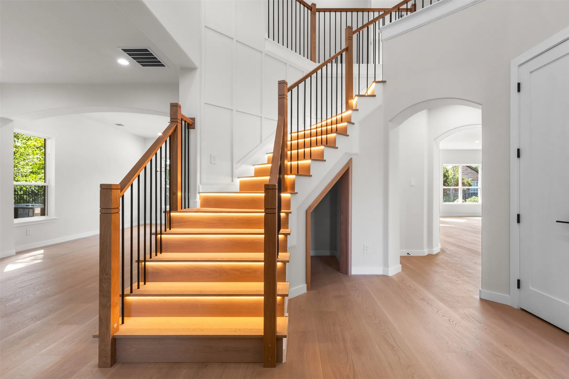 Hardwood flooring, wood staircase with black iron spindles, recessed lighting, accent wall paneling, and arched doorways