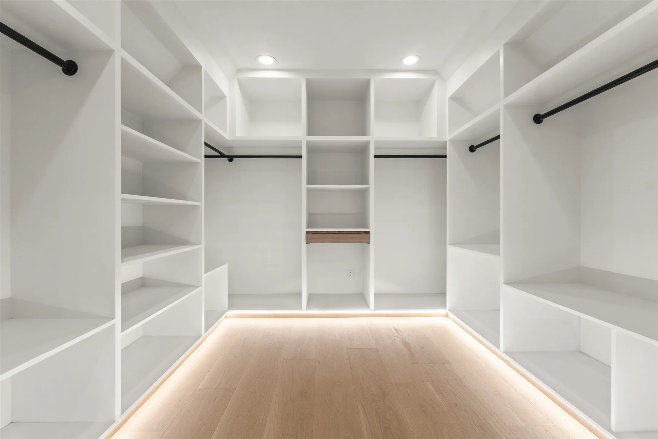 Custom built-in closet system with extensive shelving, hanging rods, recessed lighting, and wood-finish flooring