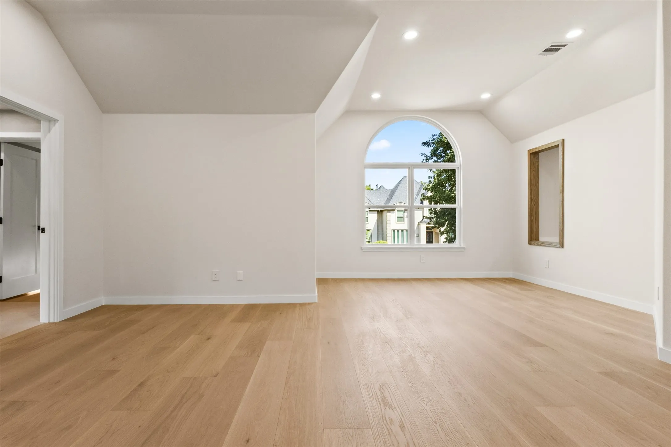 Light wood-finish flooring, vaulted ceiling, arched window, recessed lighting, and a built-in wall niche