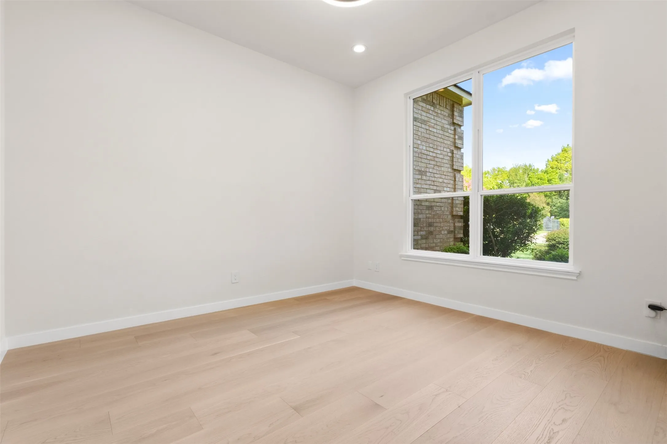 Light wood-finish flooring, recessed lighting, and a large window with white trim