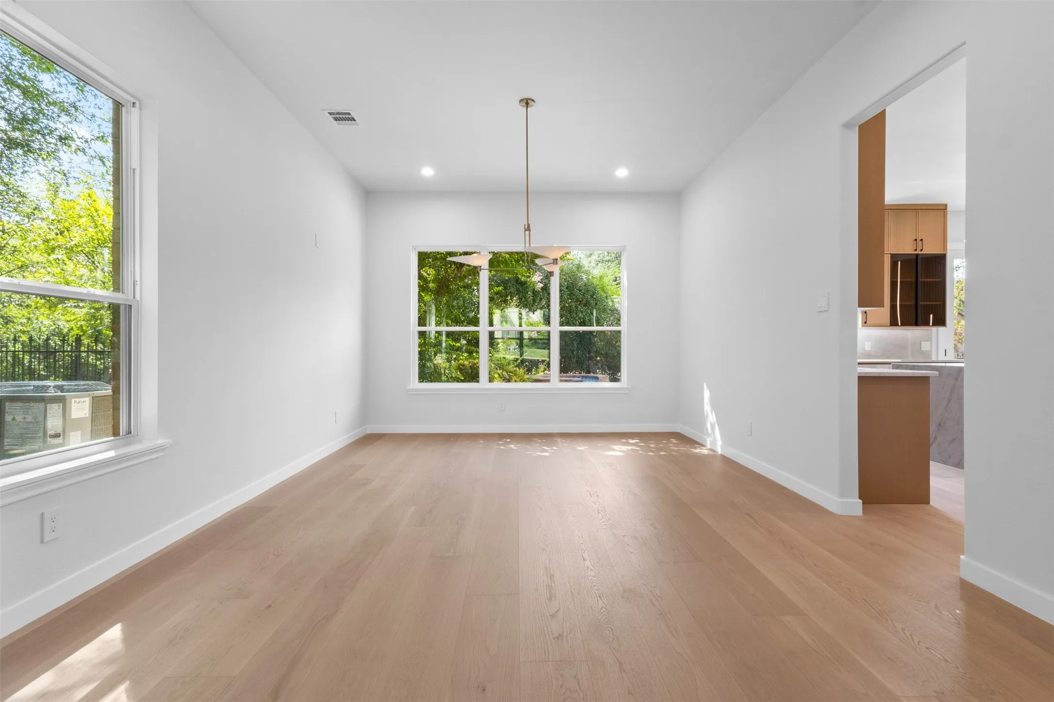 Open-concept room with light wood-finish flooring, recessed lighting, and a modern pendant light fixture