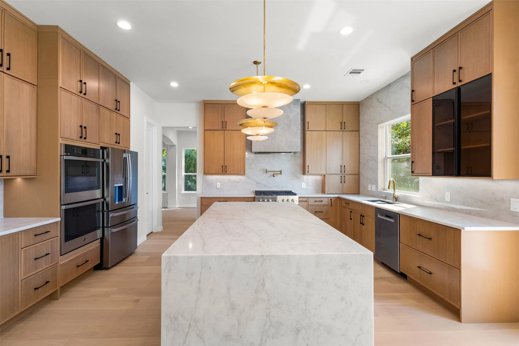 Gourmet kitchen featuring a waterfall island, custom cabinetry, integrated stainless steel appliances, and wood-finish flooring
