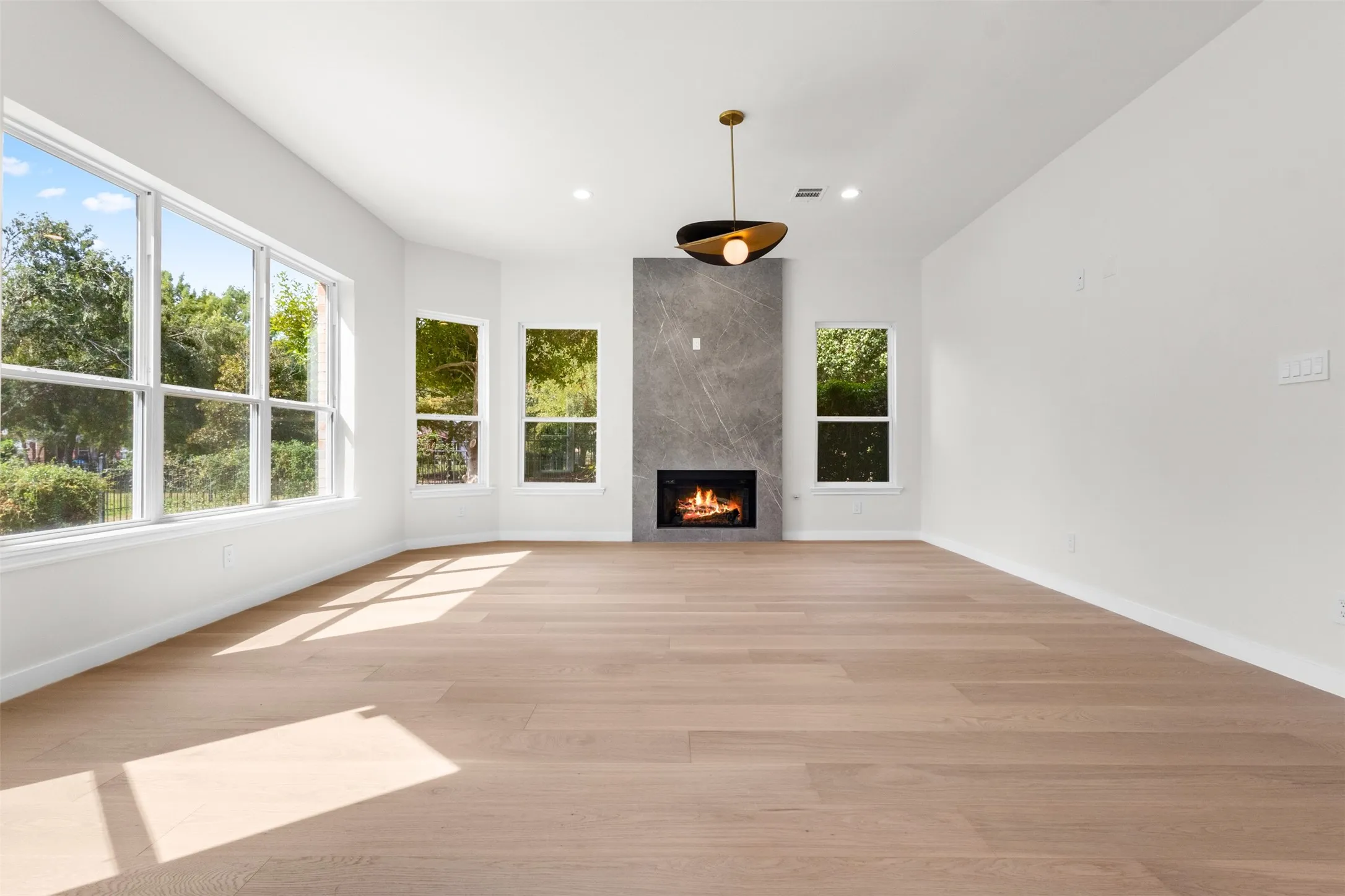 Expansive room featuring wood-finish flooring, a contemporary fireplace with a stone surround, recessed lighting, and multiple windows